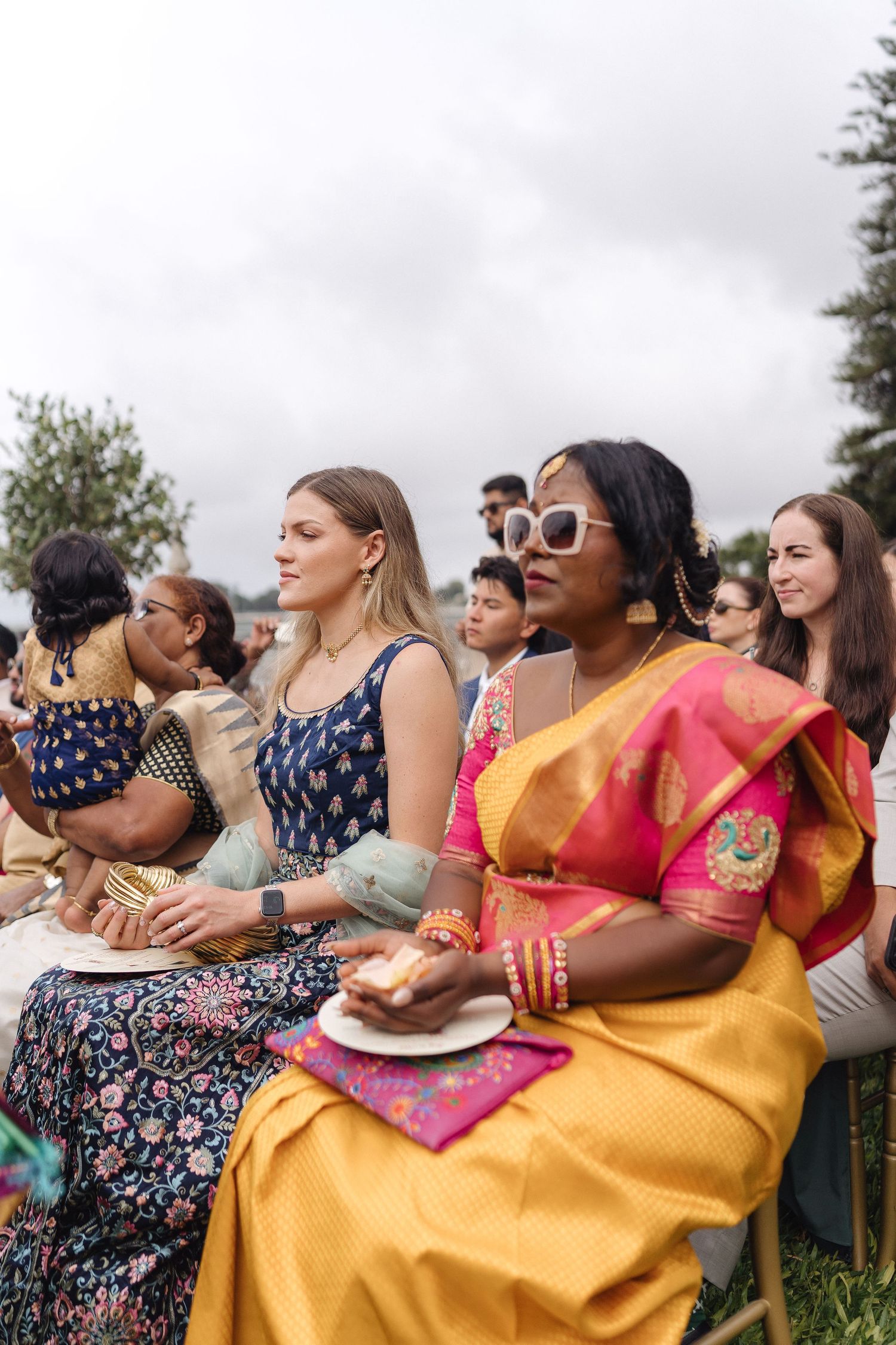 Group of guests in colorful dresses enjoying an outdoor celebration.