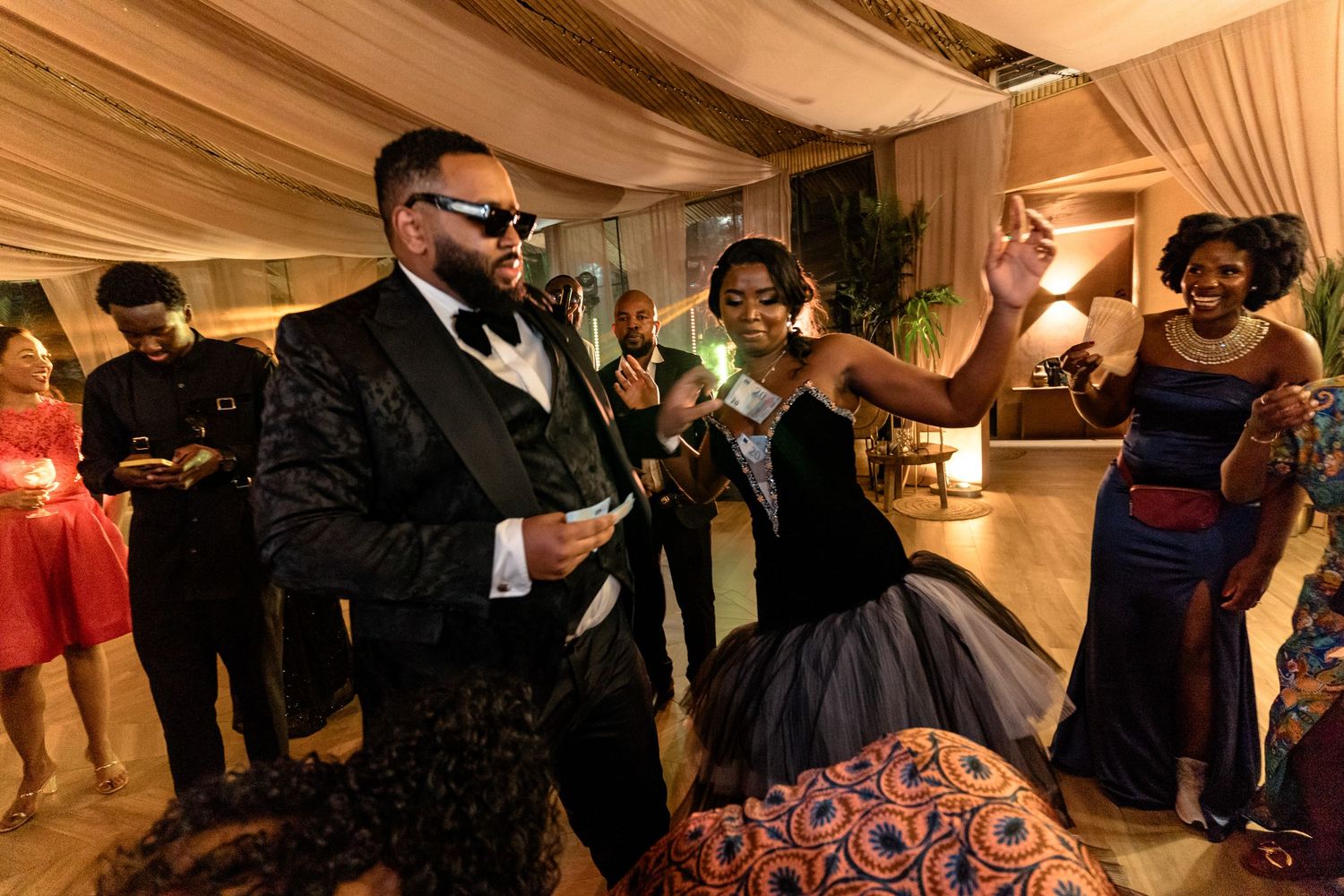 Wedding guests dancing and celebrating at an indoor reception with draped fabric ceiling decor.