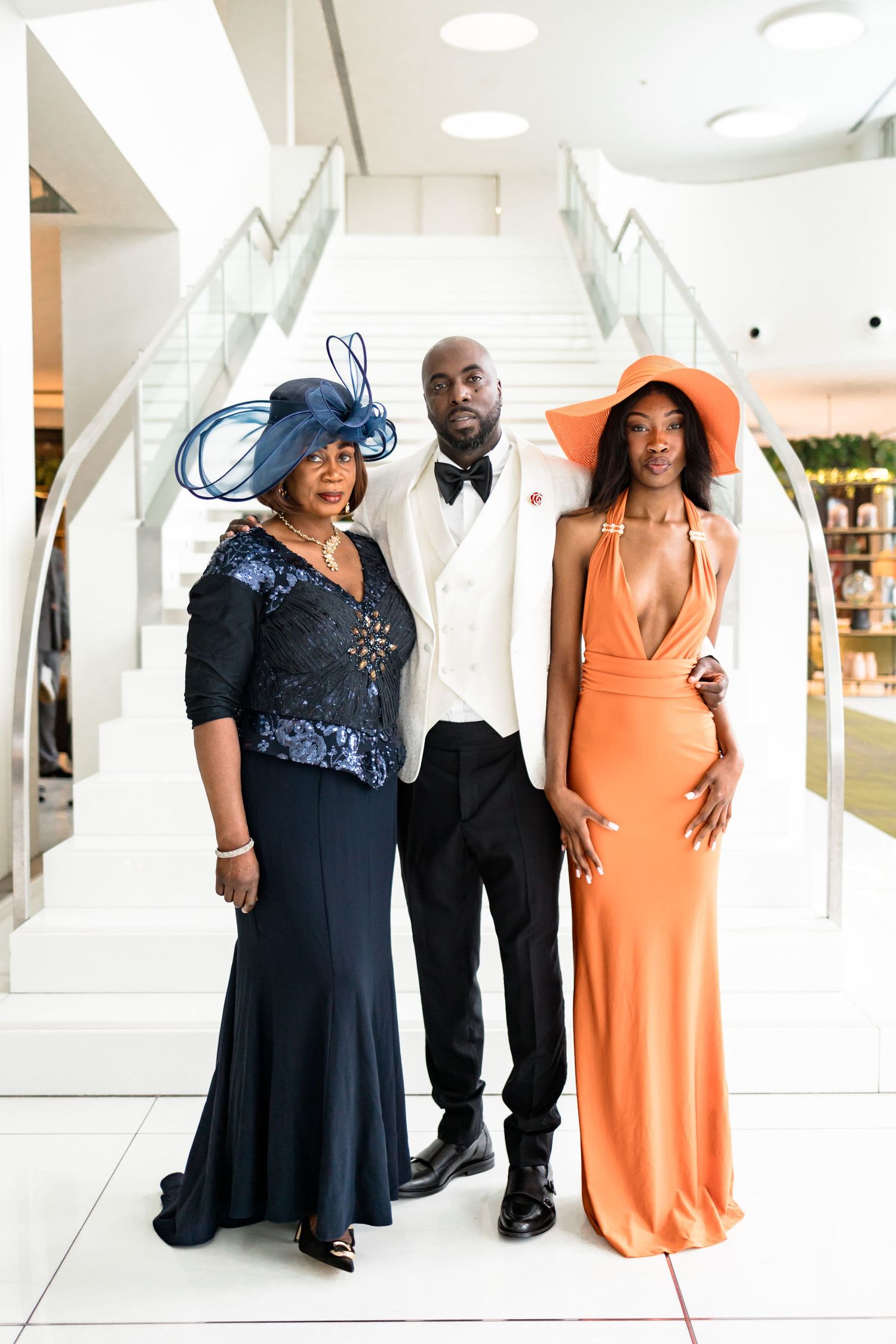 Wedding party members in navy blue and coral orange dresses pose elegantly in a bright indoor venue.