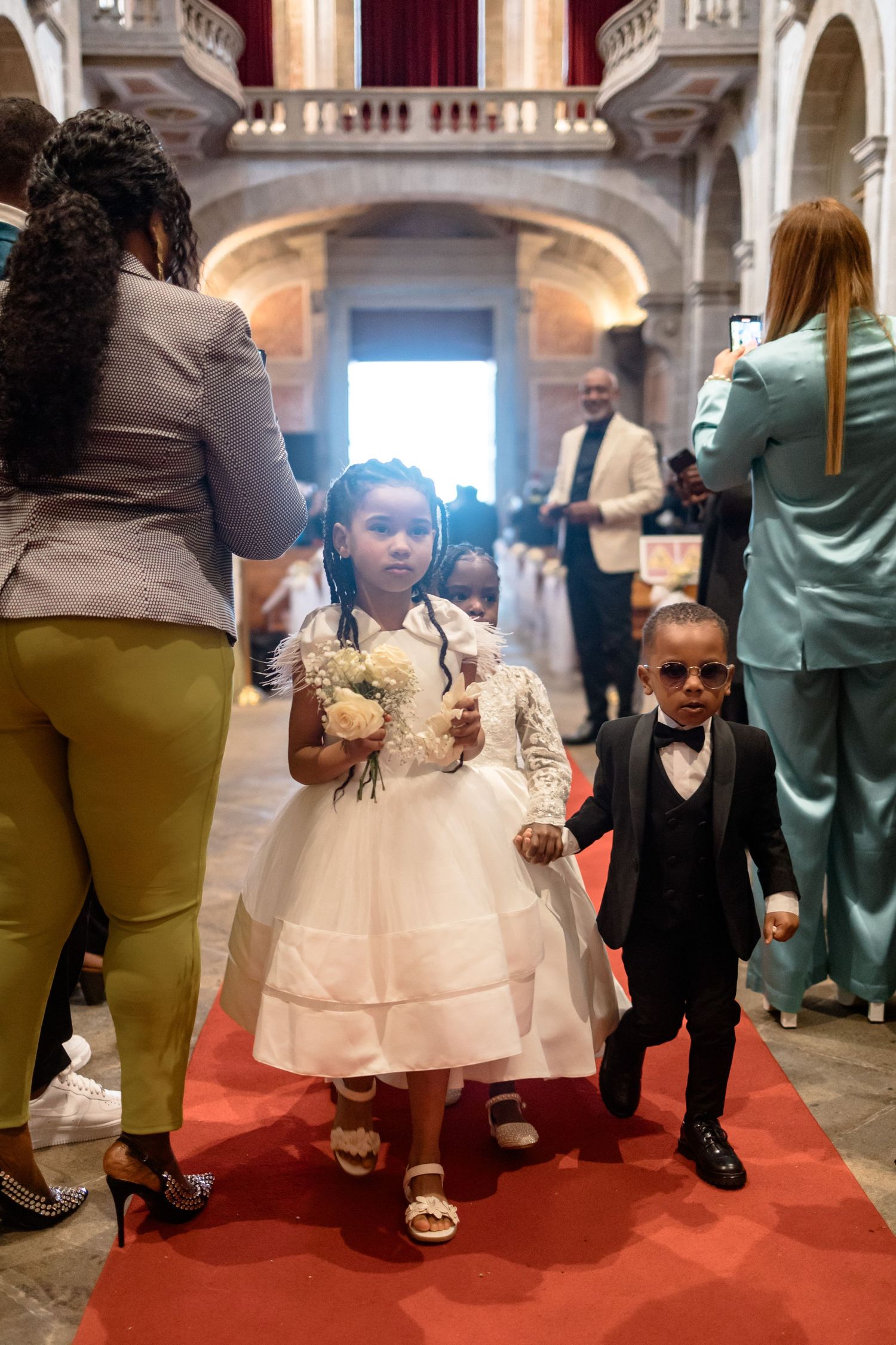 Two children walking down a red carpet in formal attire during an elegant church ceremony.
