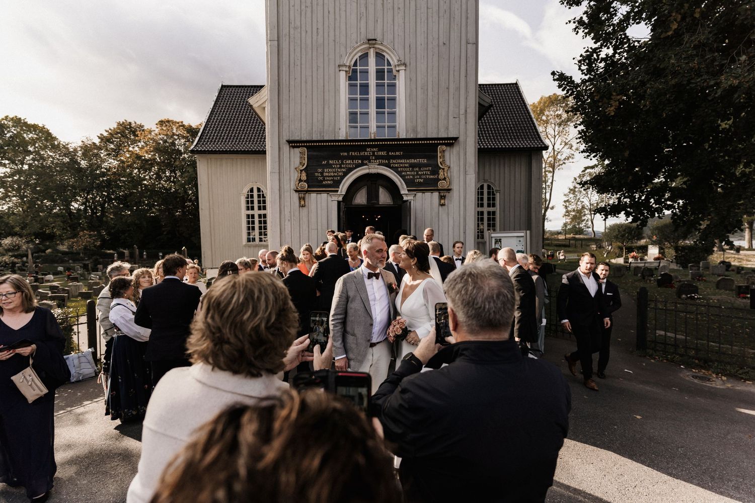 Wedding guests gathered outside a rustic wooden church building.