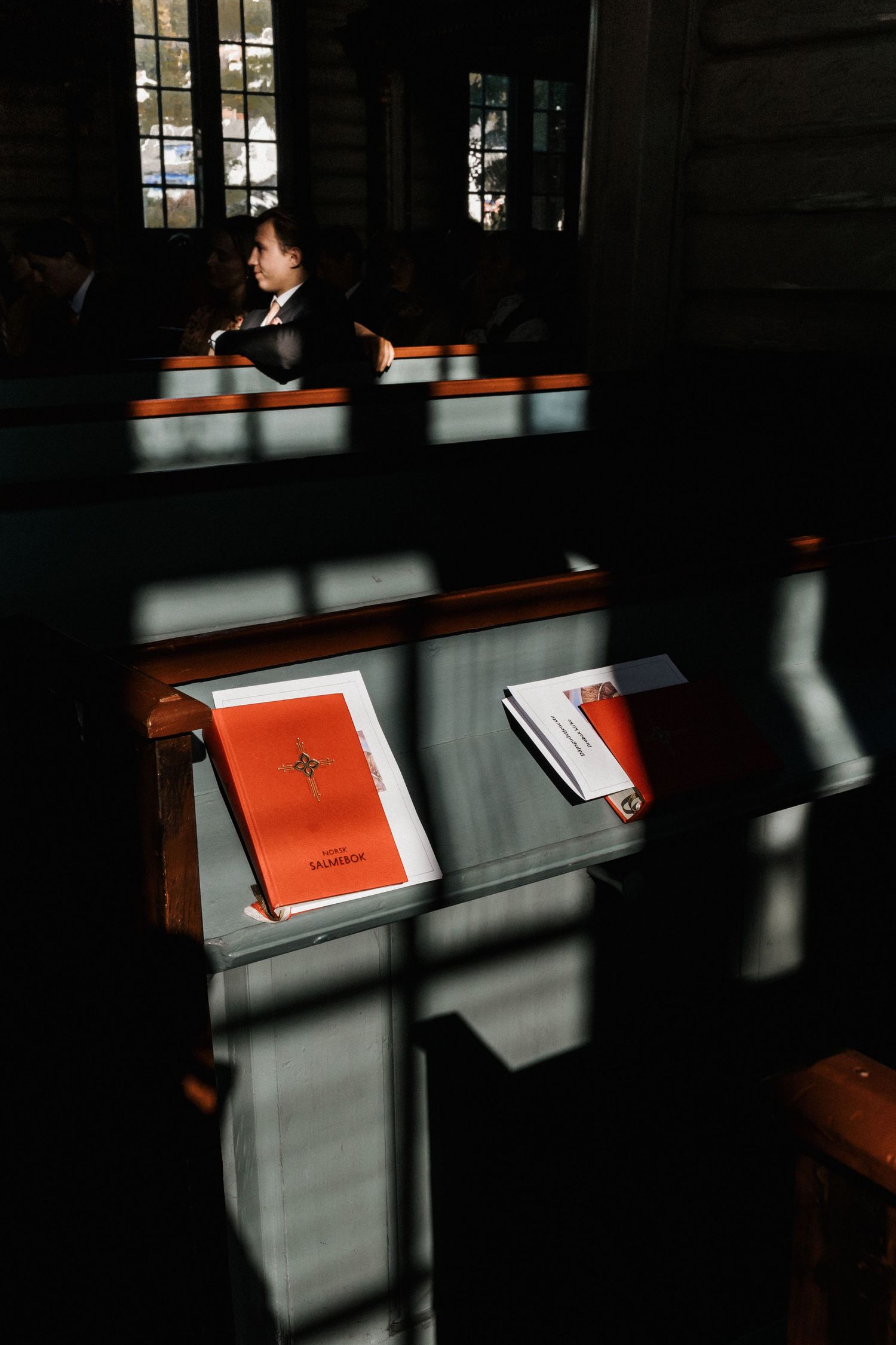 Red hymnals arranged on dark wooden church pews with dramatic shadows.