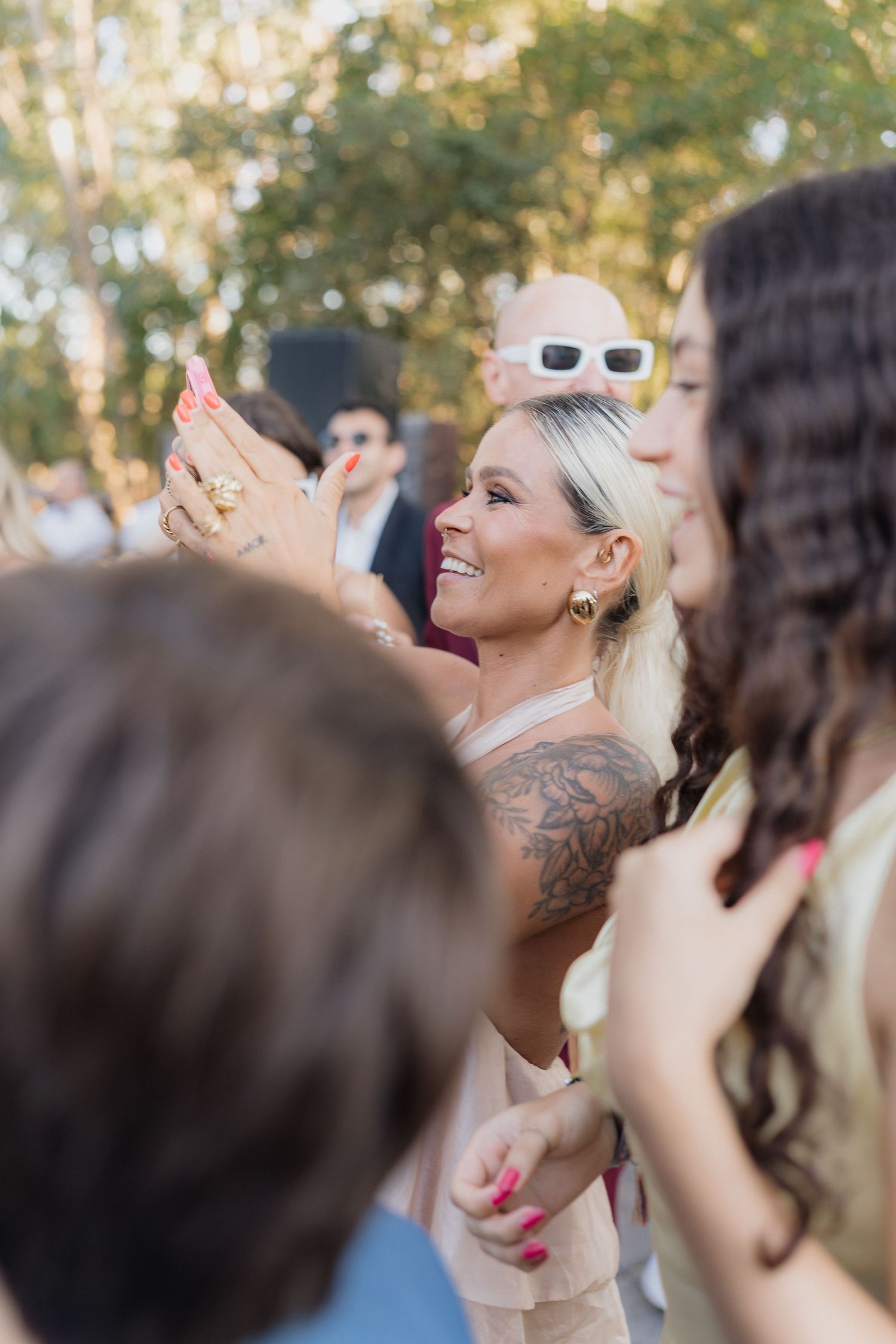 Crowd of wedding guests dancing with hands in the air during outdoor celebration.