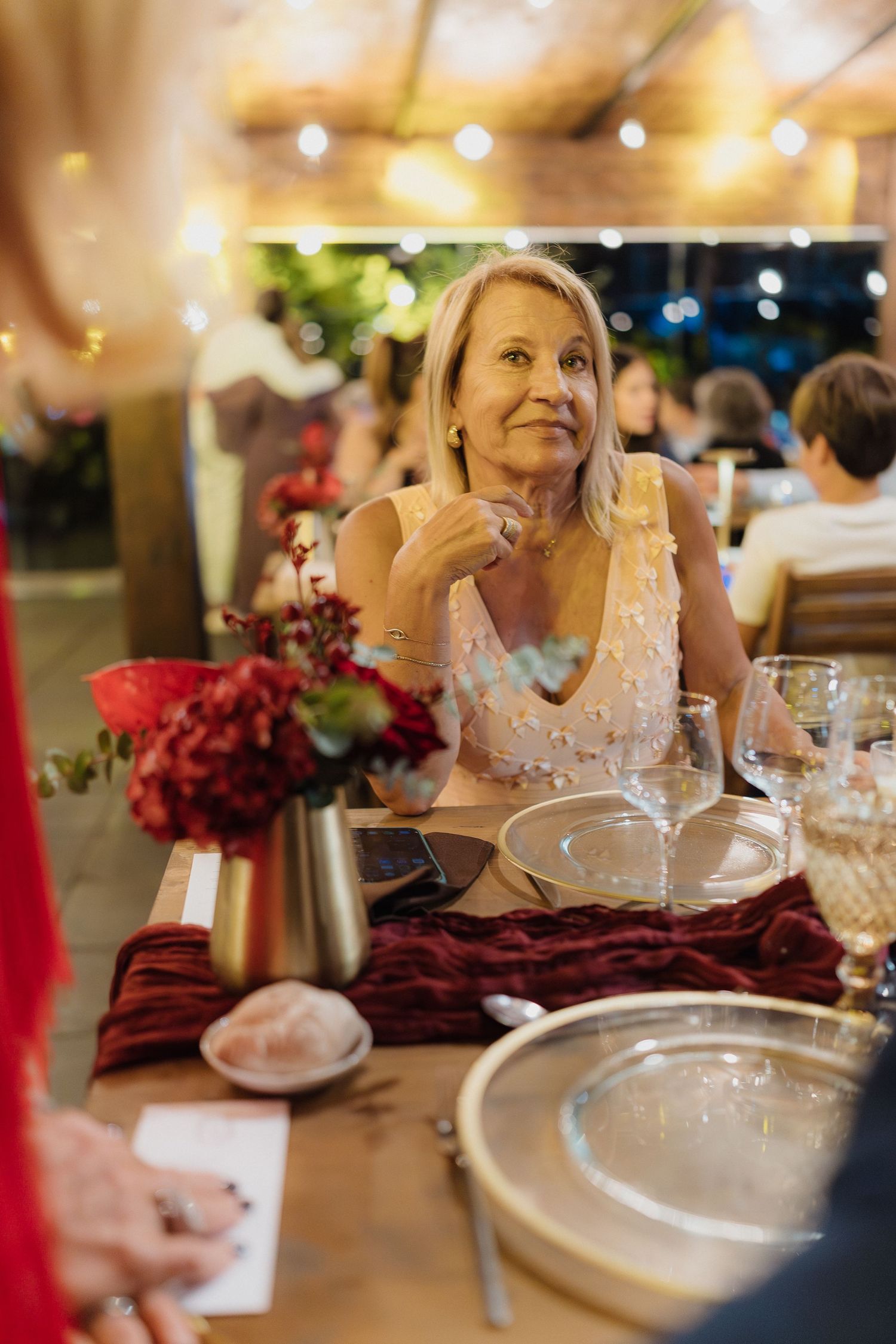 Elegant table settings at a wedding reception with burgundy floral centerpieces and glowing ambient lighting.