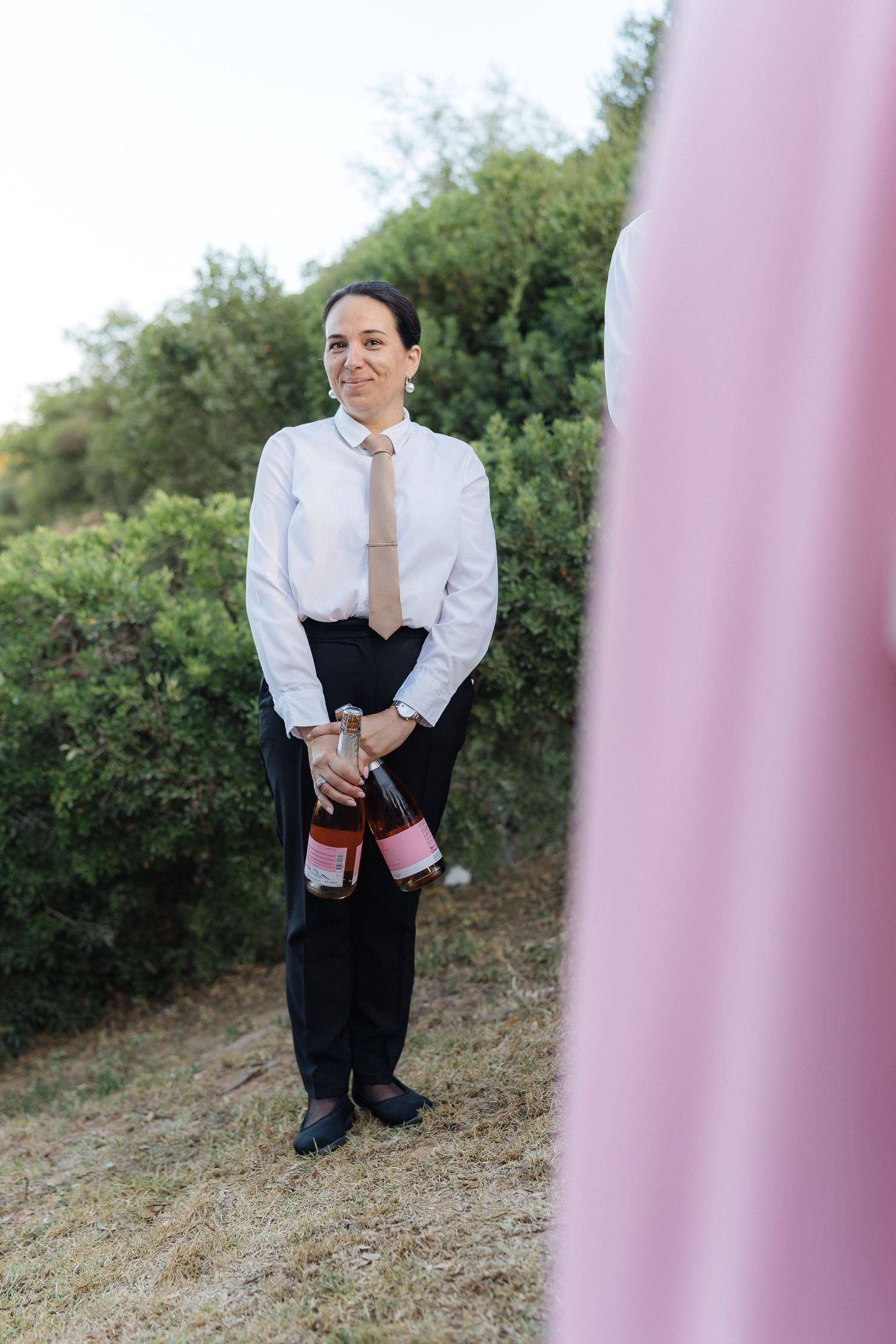 Wedding guest in formal attire posing against pink backdrop outdoors.