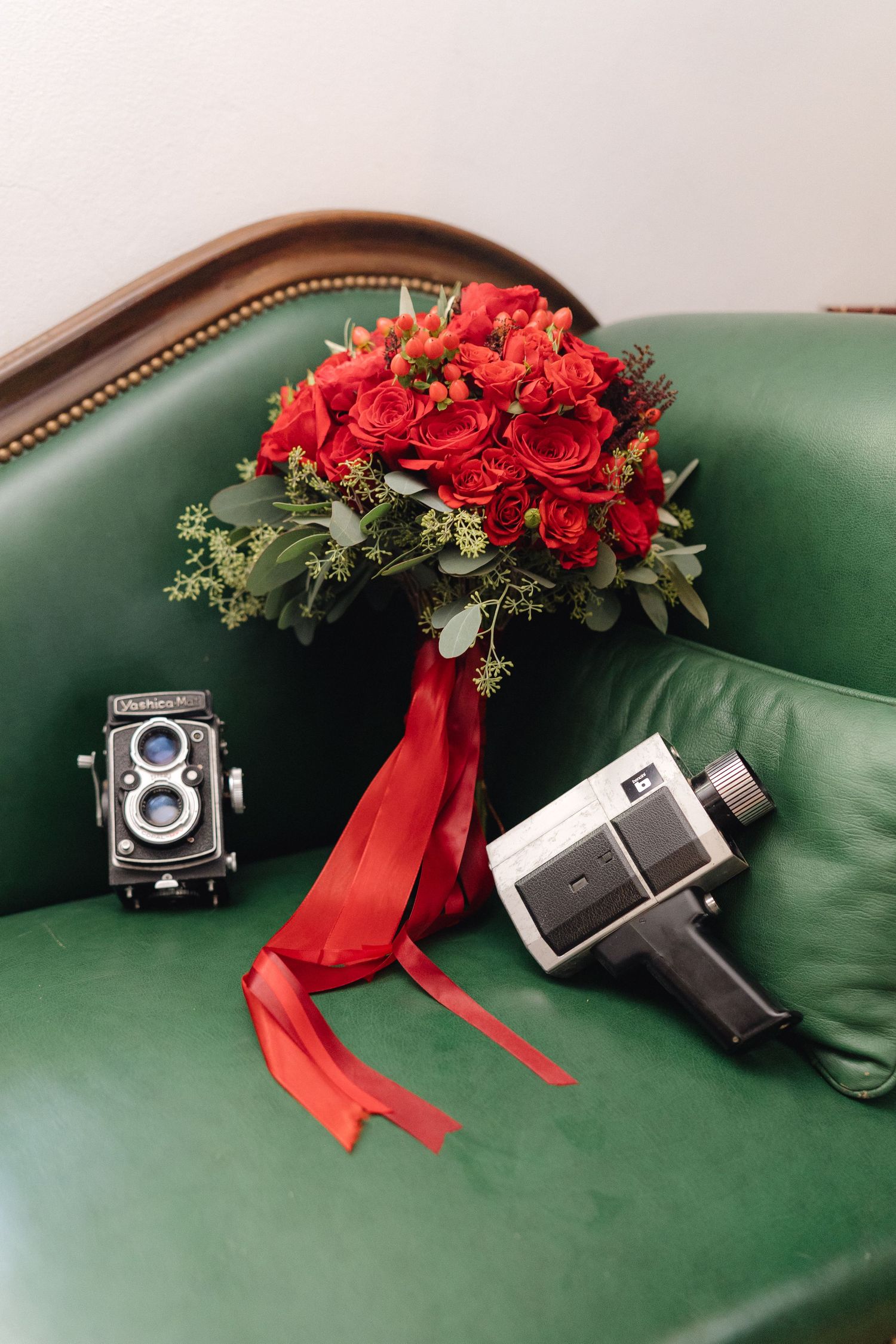 Vintage cameras and red floral arrangement displayed on a green velvet couch.