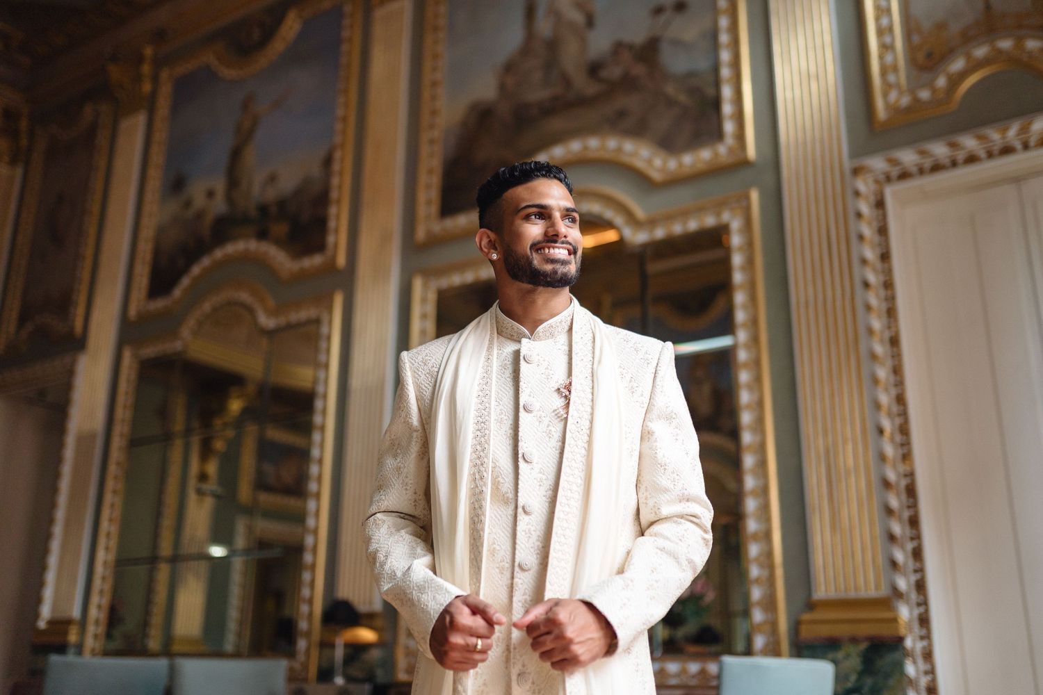 Person wearing elegant cream traditional Indian wedding attire in ornate room with gilded details.