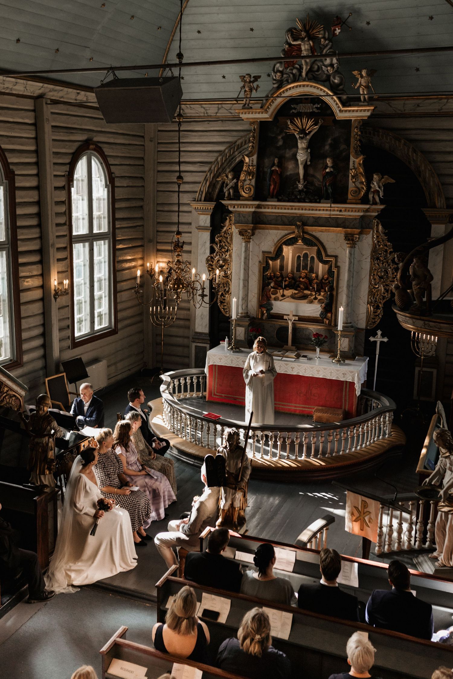 Historic wooden church interior with ornate altar and pews during a wedding ceremony.