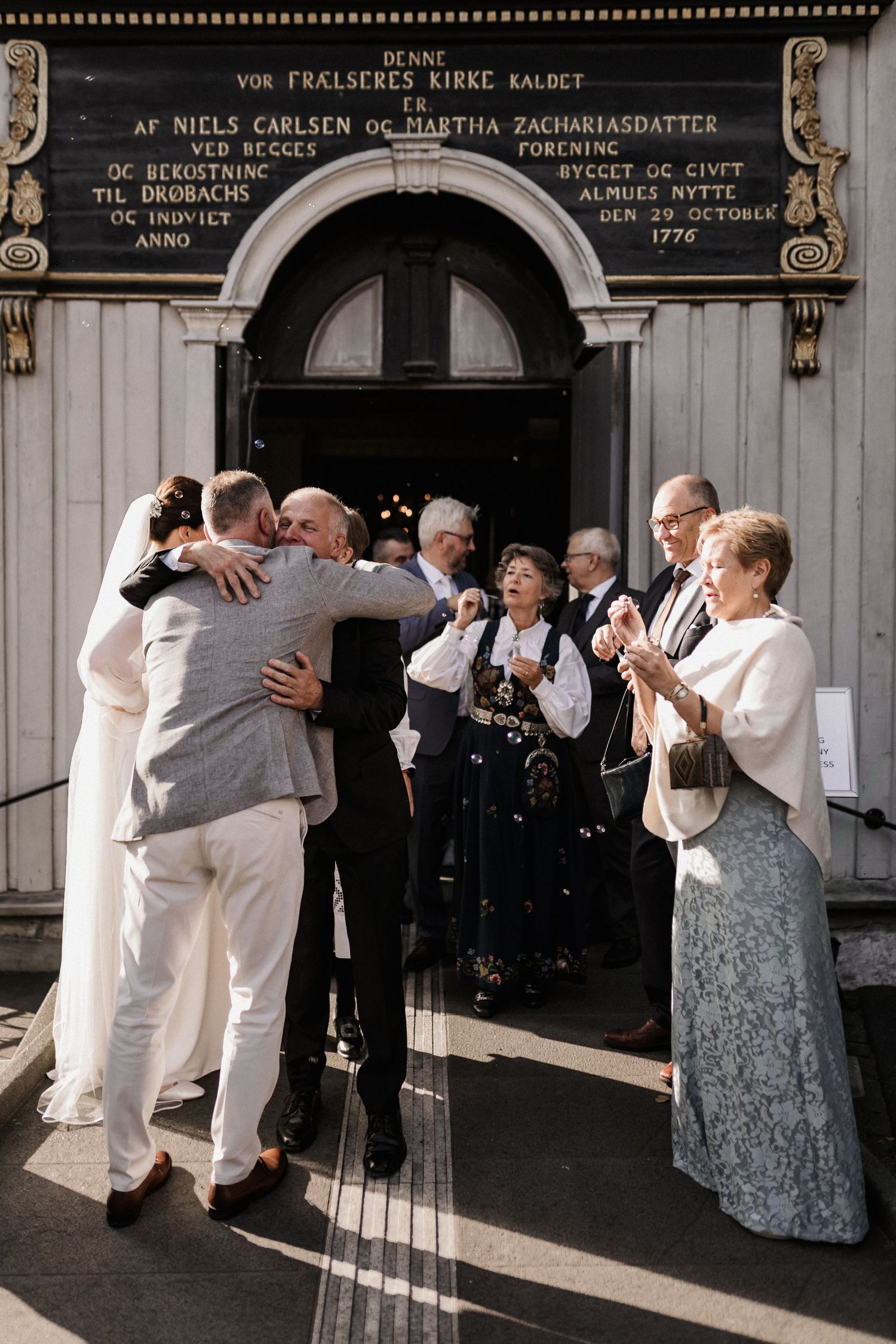 Wedding celebration outside historic building with guests greeting and embracing.