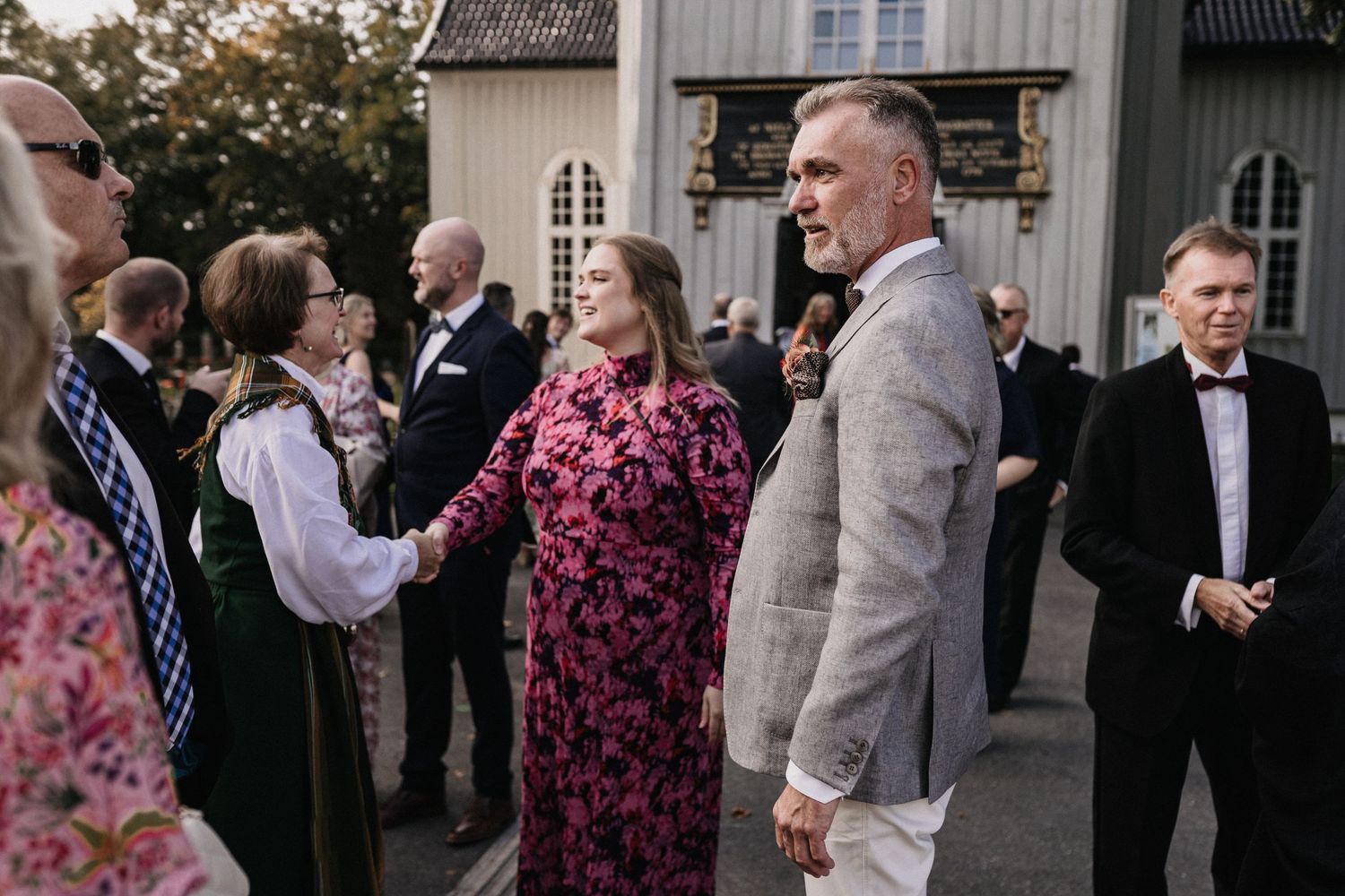 Wedding guests mingle and socialize outside a traditional white church building during a celebration.