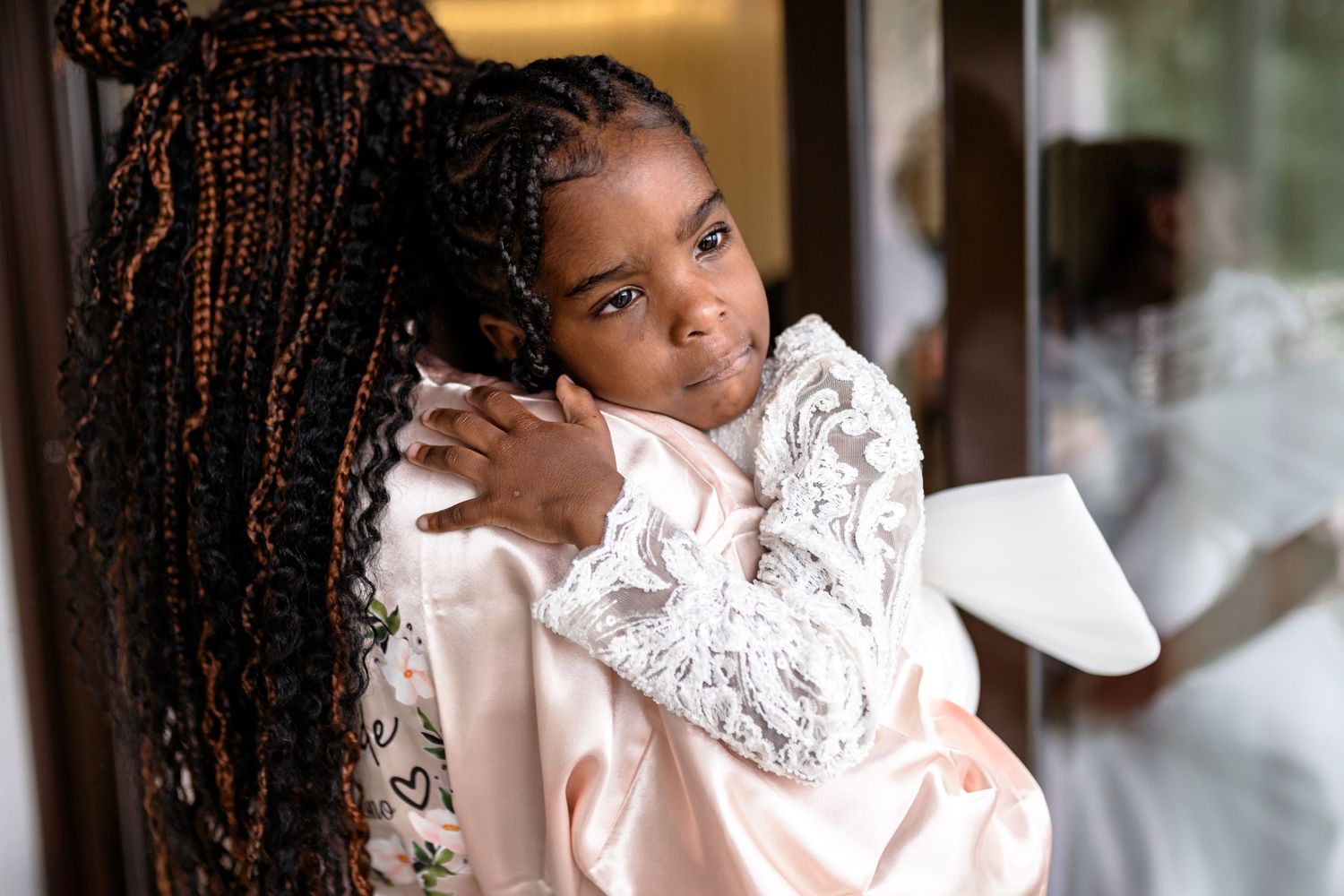 Young person in lace robe posing near window with long braided hair.
