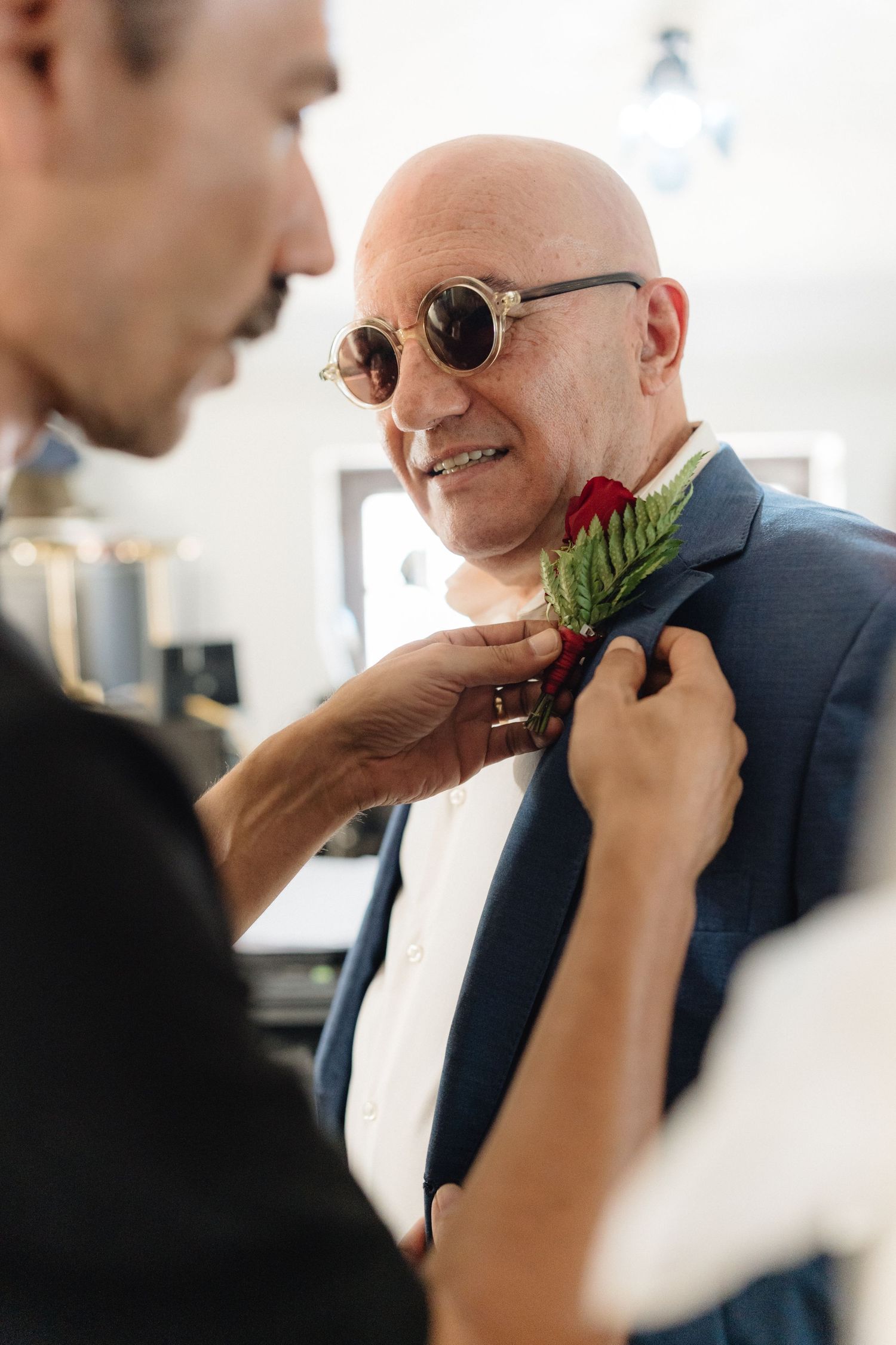 Someone adjusts a boutonniere with greenery on a suit jacket in bright natural light.