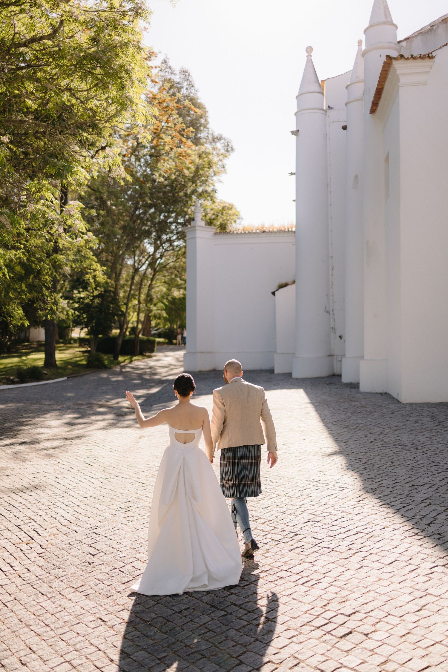 Couple walking hand in hand along cobblestone path beside white church building.