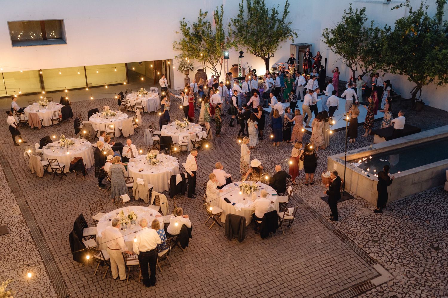 Overhead view of an outdoor wedding reception with round tables and string lights.
