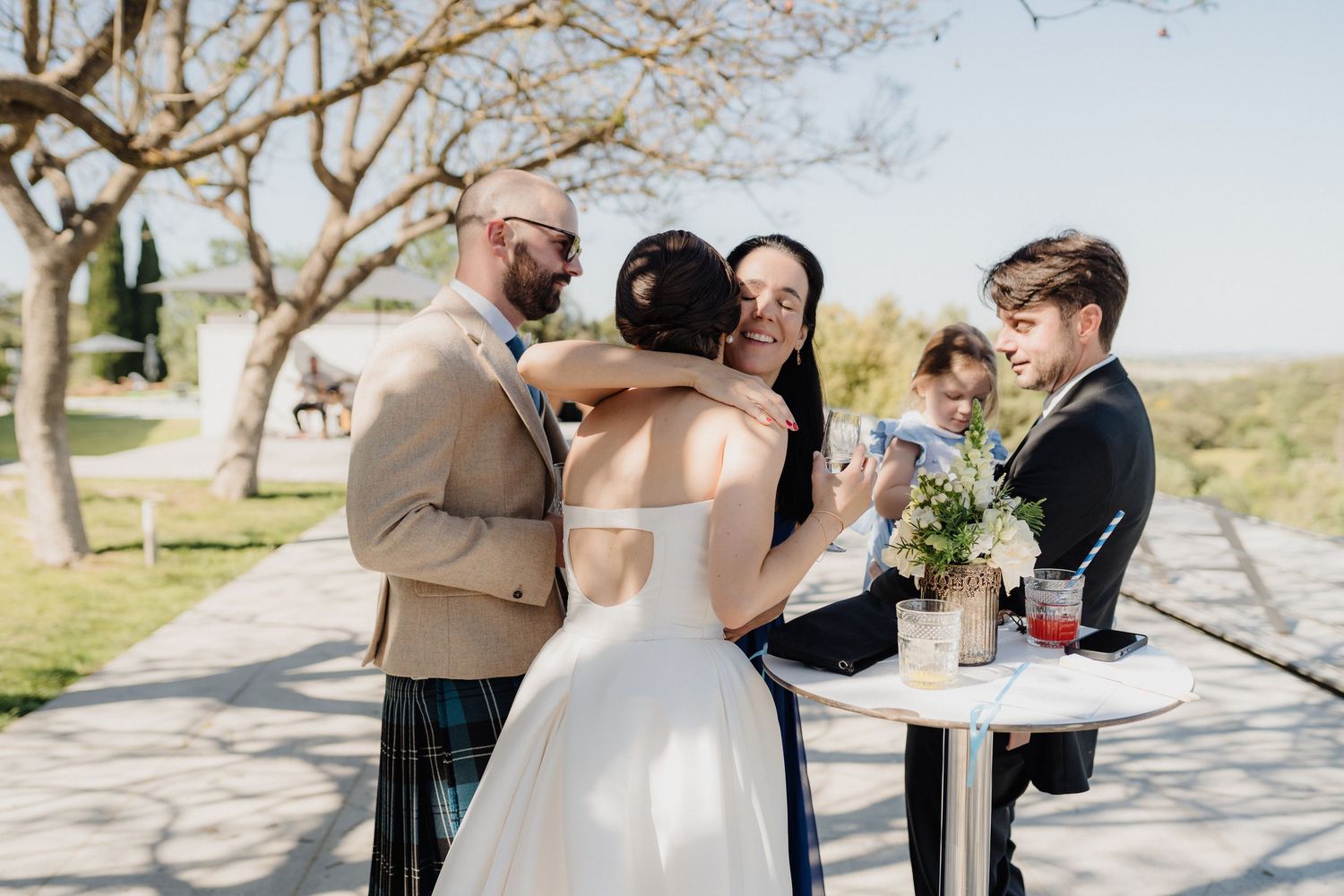 A wedding celebration moment captured outdoors with guests gathered around a small table.