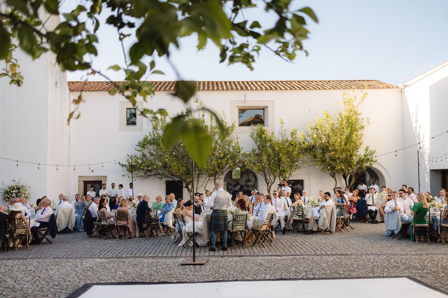 Wide view of a courtyard wedding reception with white buildings and string lights.