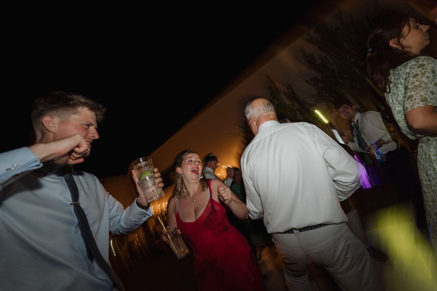 Partygoers dancing enthusiastically in a dark room with colorful spotlights.
