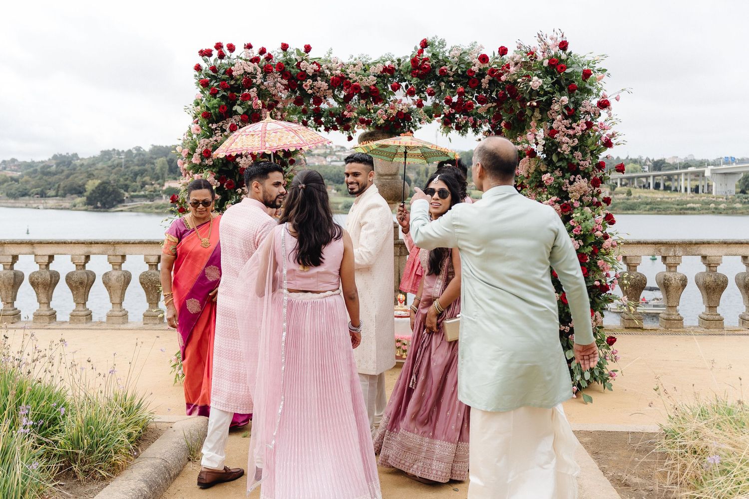 Outdoor wedding ceremony under a floral arch decorated with red and pink roses.
