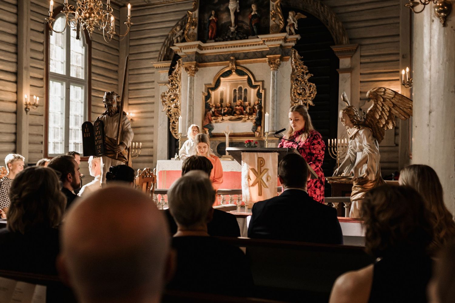 Traditional church sanctuary with wooden walls and decorative chandeliers during a ceremony.