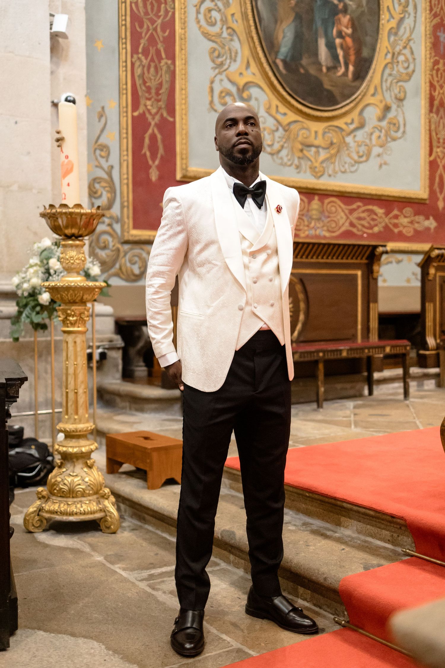Elegant groom in white tuxedo jacket standing in ornate church interior.