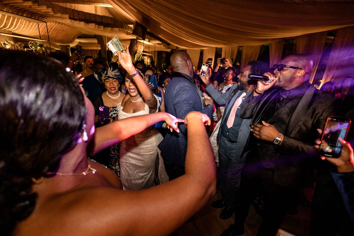 Wedding reception dance floor filled with guests celebrating under draped fabric ceiling.