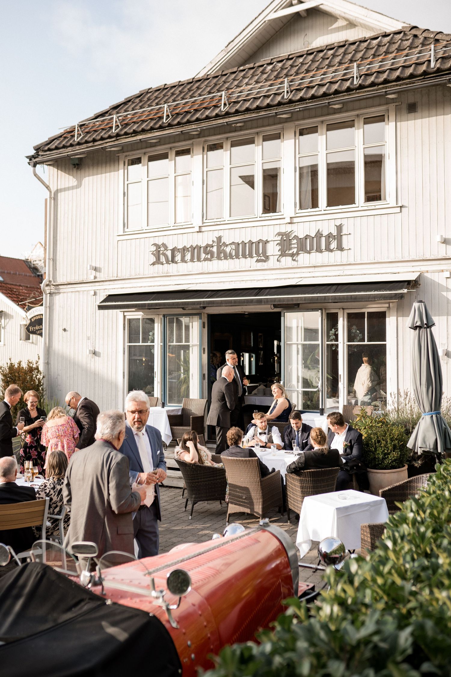 Guests mingle outside a traditional white hotel building during a wedding reception.
