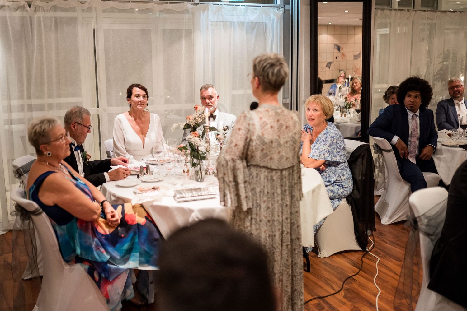 Wedding reception scene showing guests seated at decorated tables with white linens.