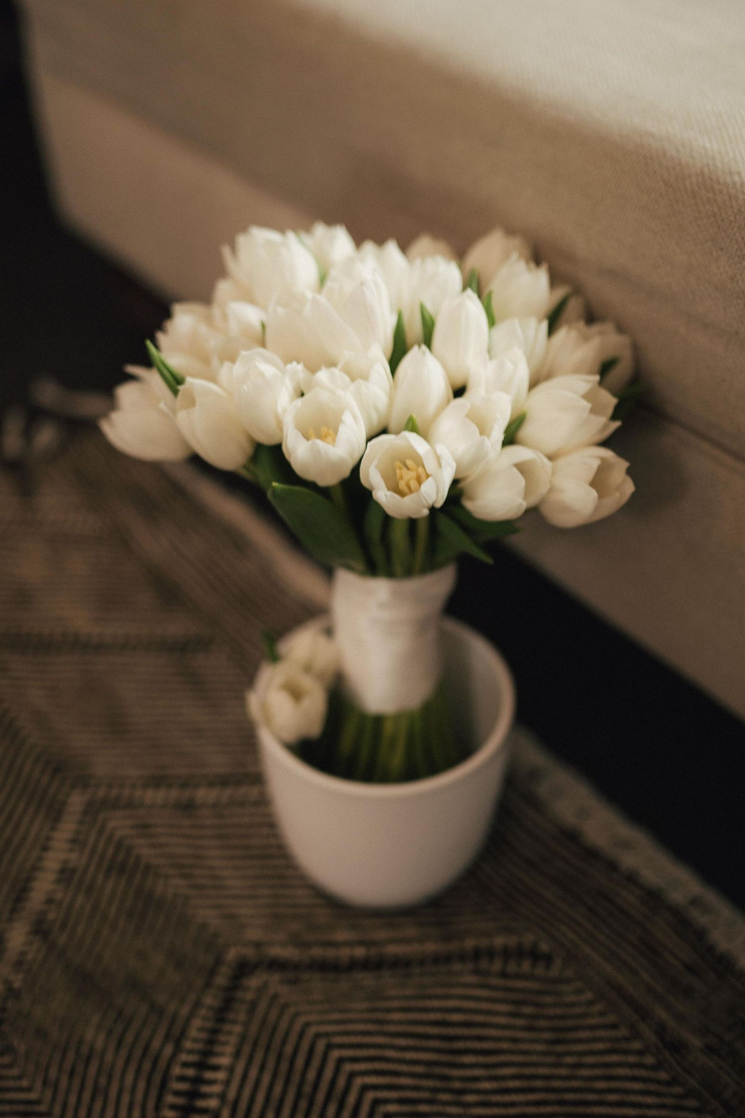 White tulips arranged in a small ceramic vase on a textured surface.