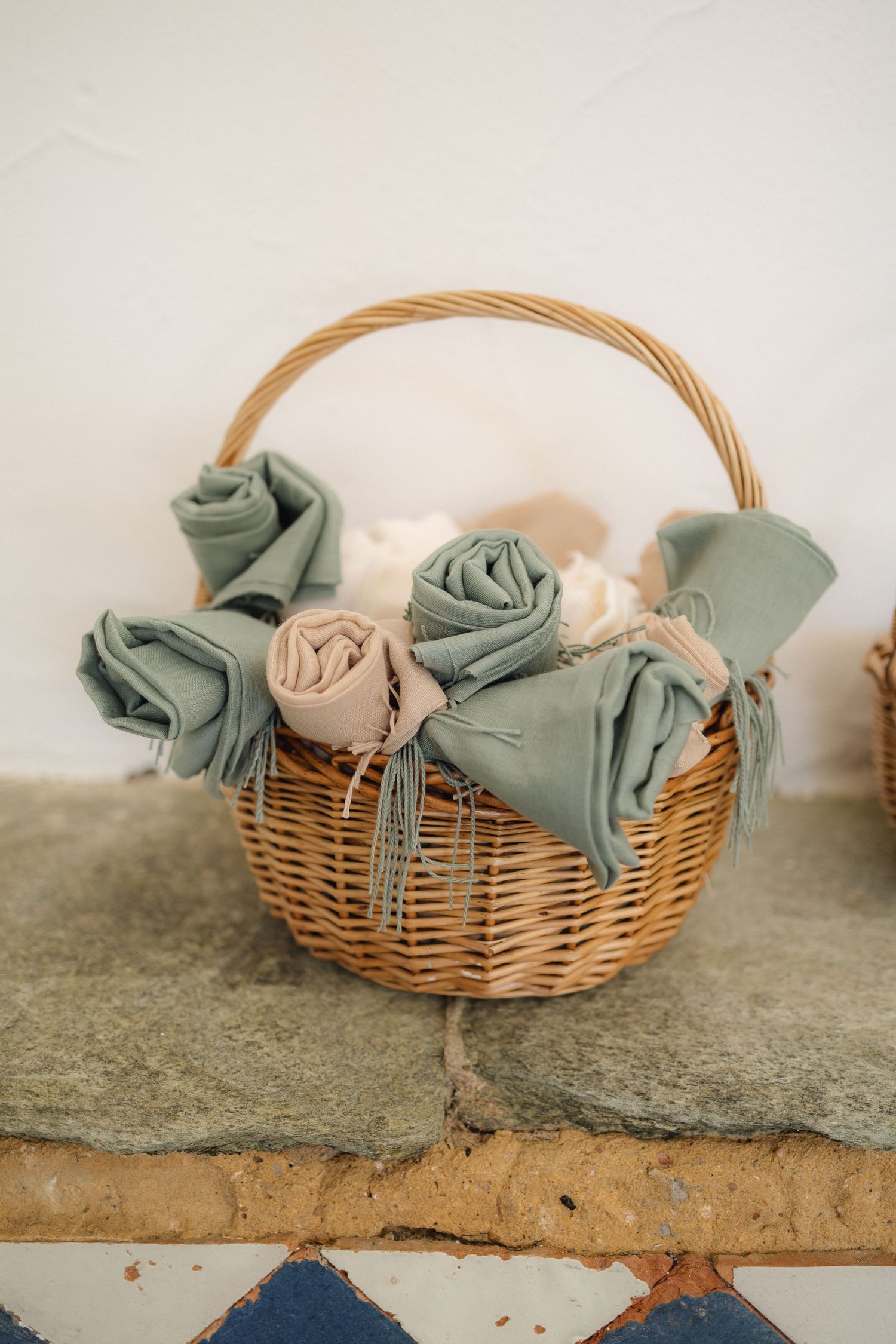 Woven basket filled with folded sage and neutral colored napkins.