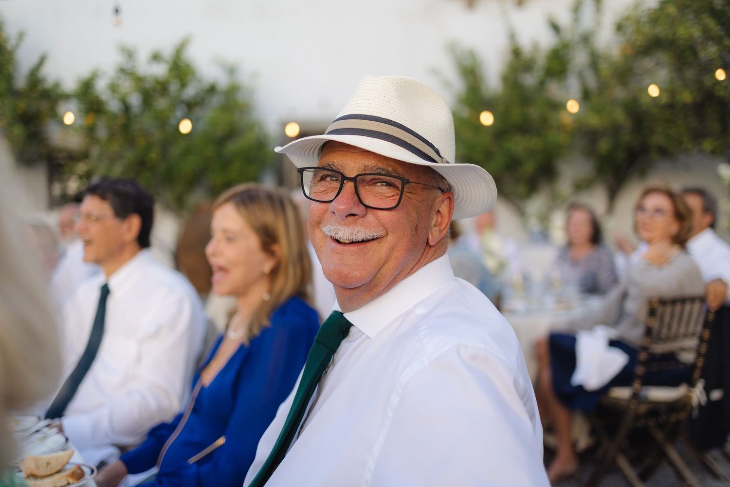 Wedding guests enjoying an outdoor reception at sunset with string lights overhead.