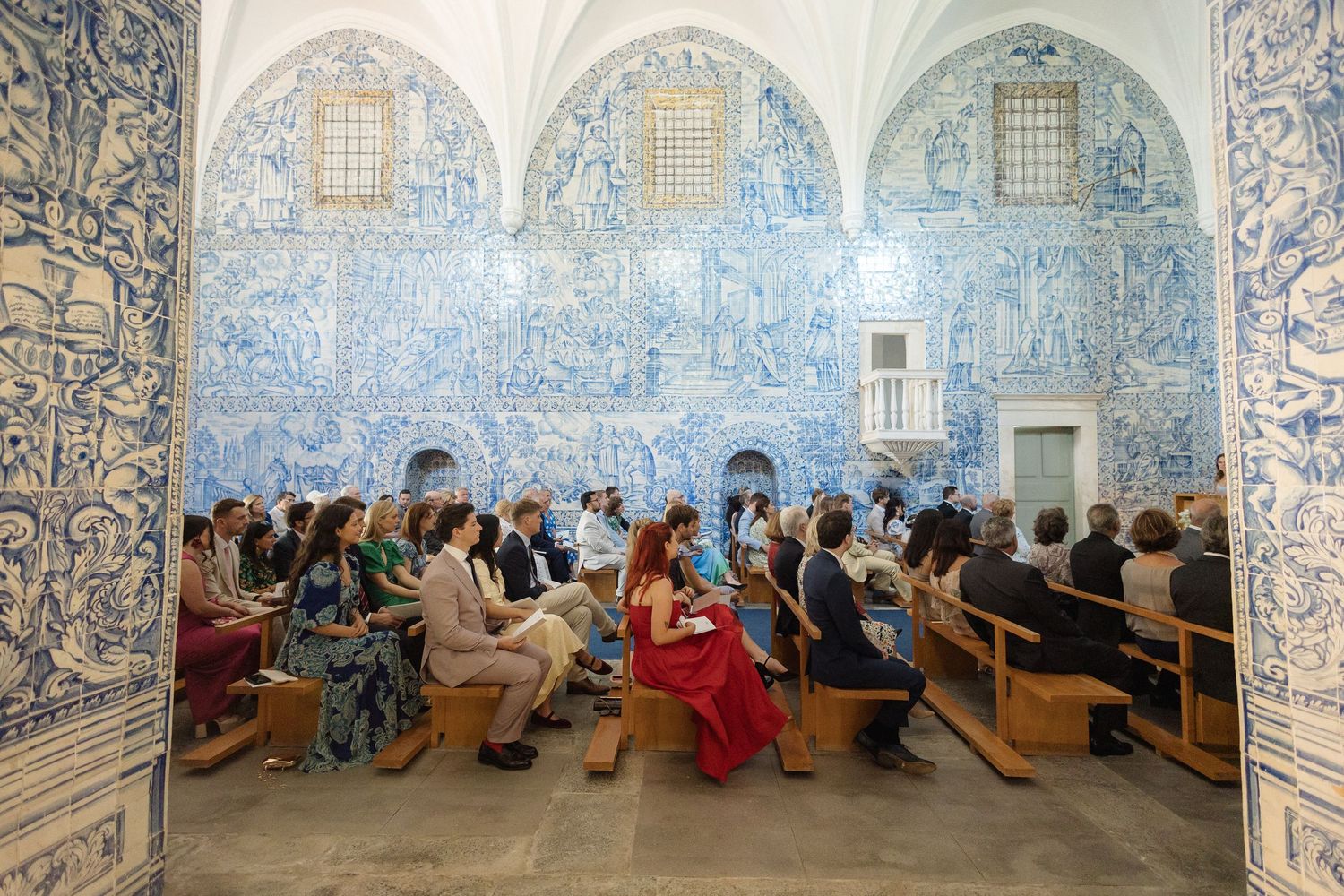 Wide angle view of wedding guests seated in a historic Portuguese chapel with blue tiled walls.