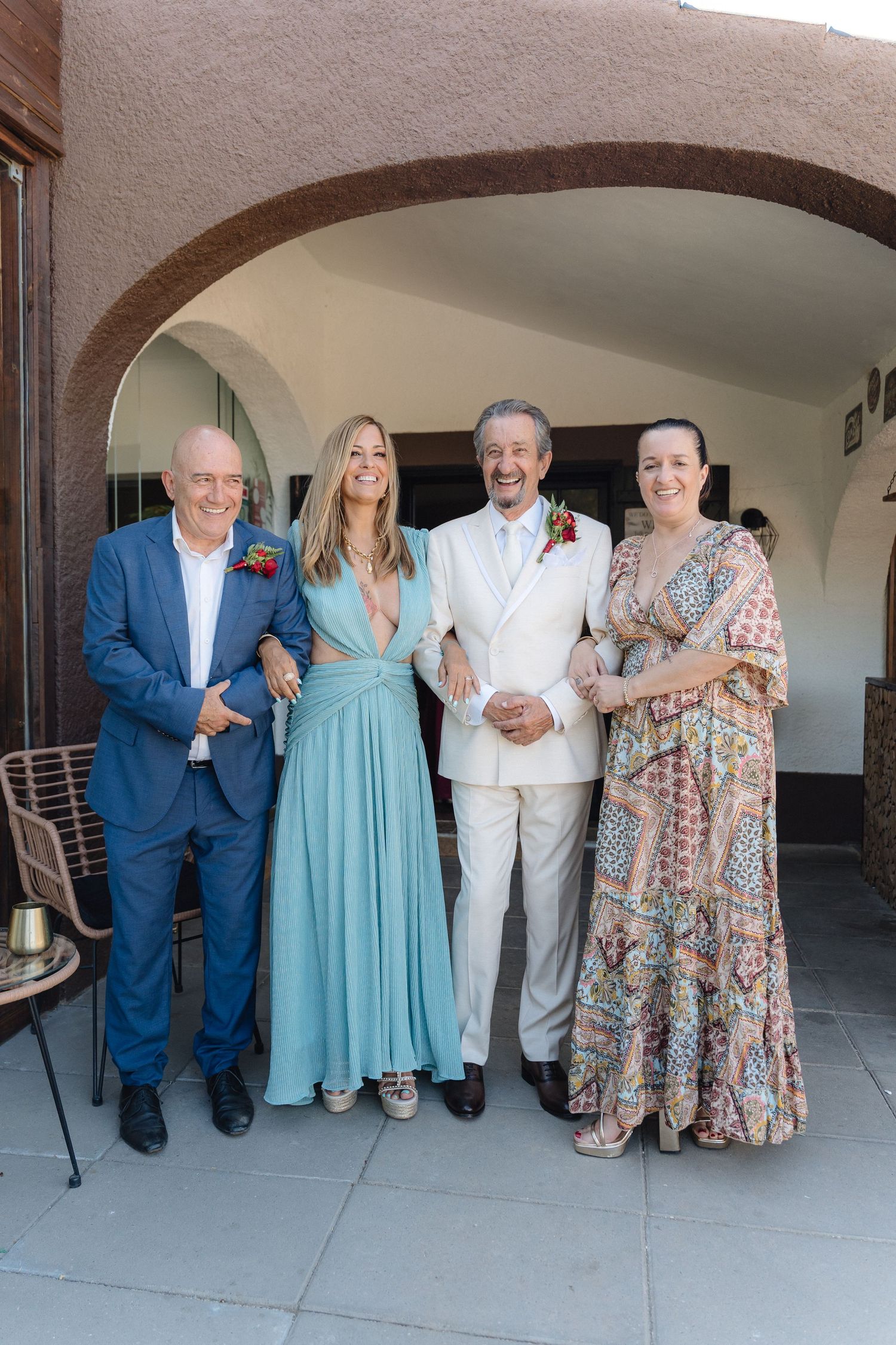 Wedding party poses together against a stucco wall in formal attire.