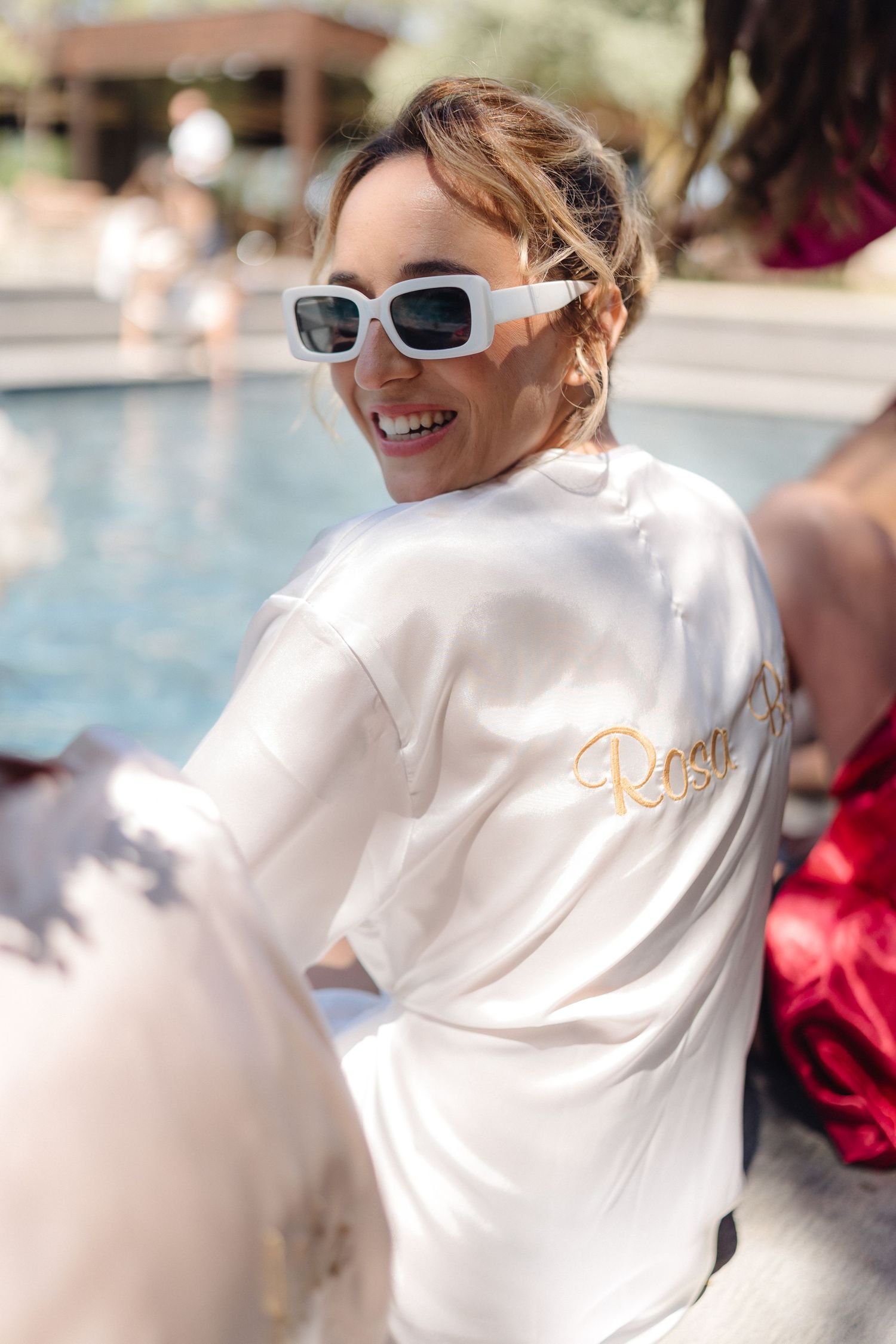 Person in white robe and sunglasses lounging by pool with embroidered text visible.