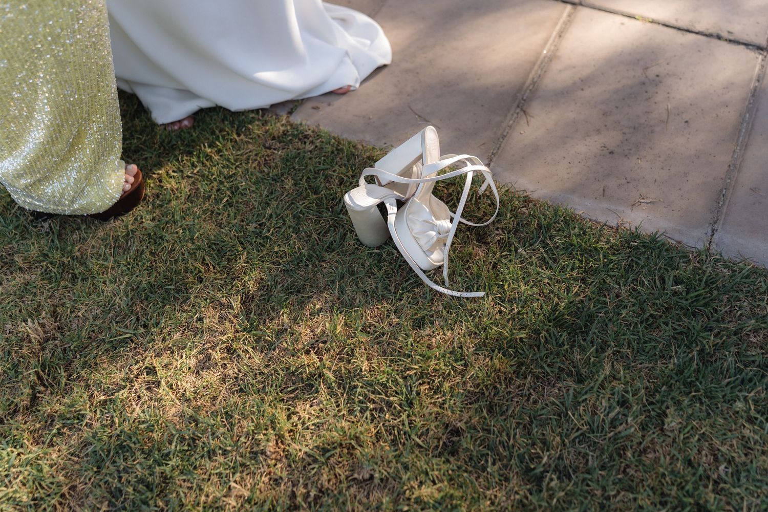 Close-up detail shot of wedding dress hem and shoes on grassy ground.