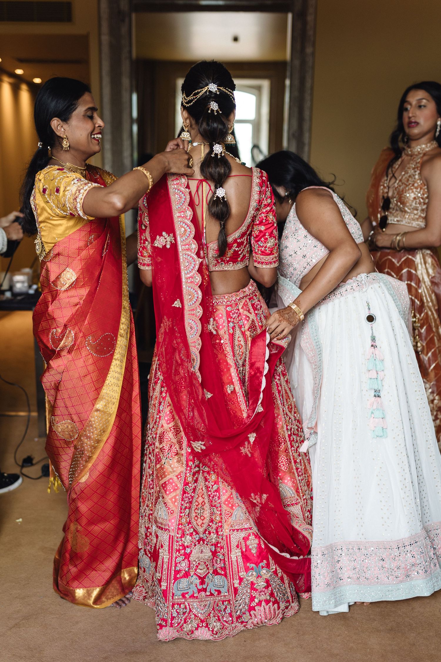 Group wearing colorful Indian wedding attire including red lehengas and white and coral sarees.