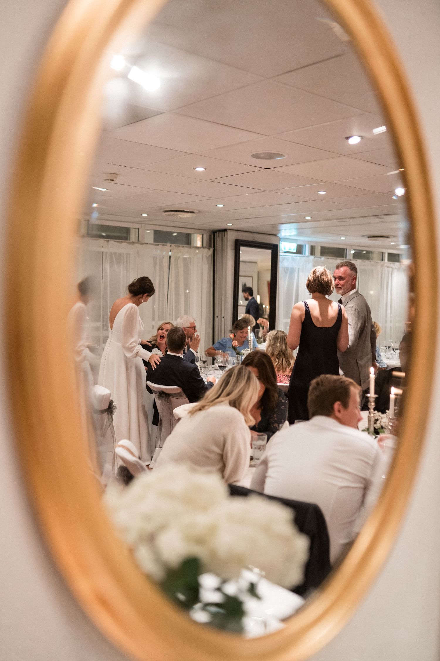 Elegant banquet room viewed through golden circular mirrors showing guests and white table settings.