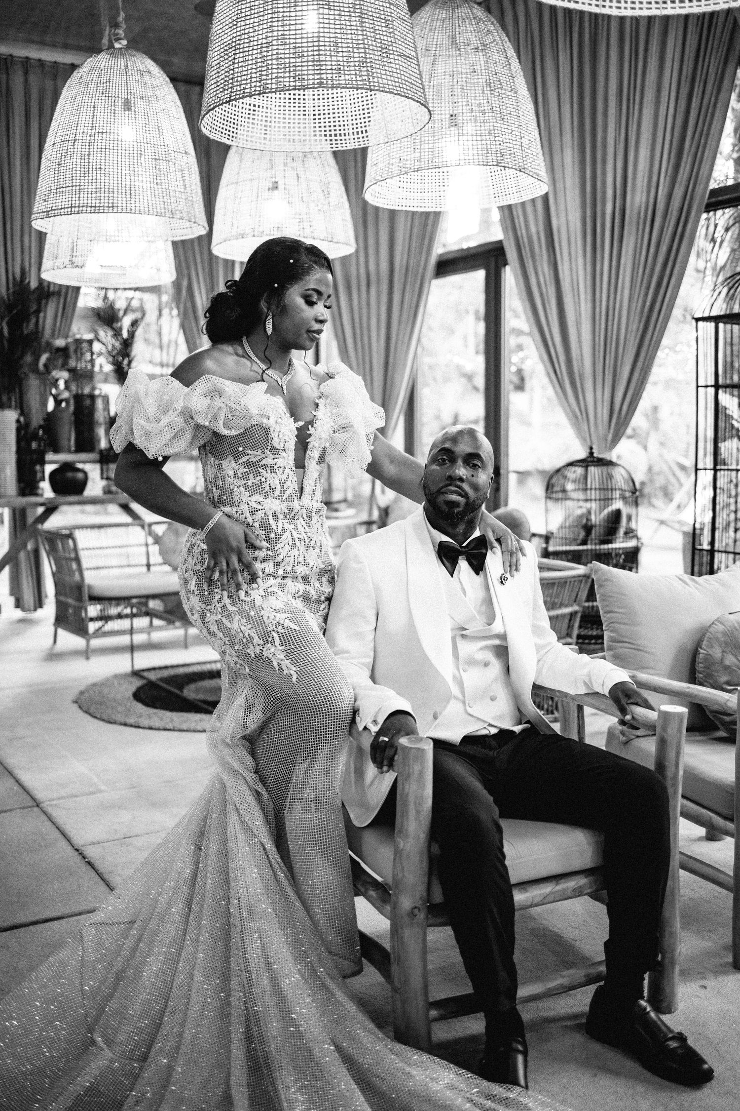Black and white photo of couple in formal attire under crystal chandeliers.