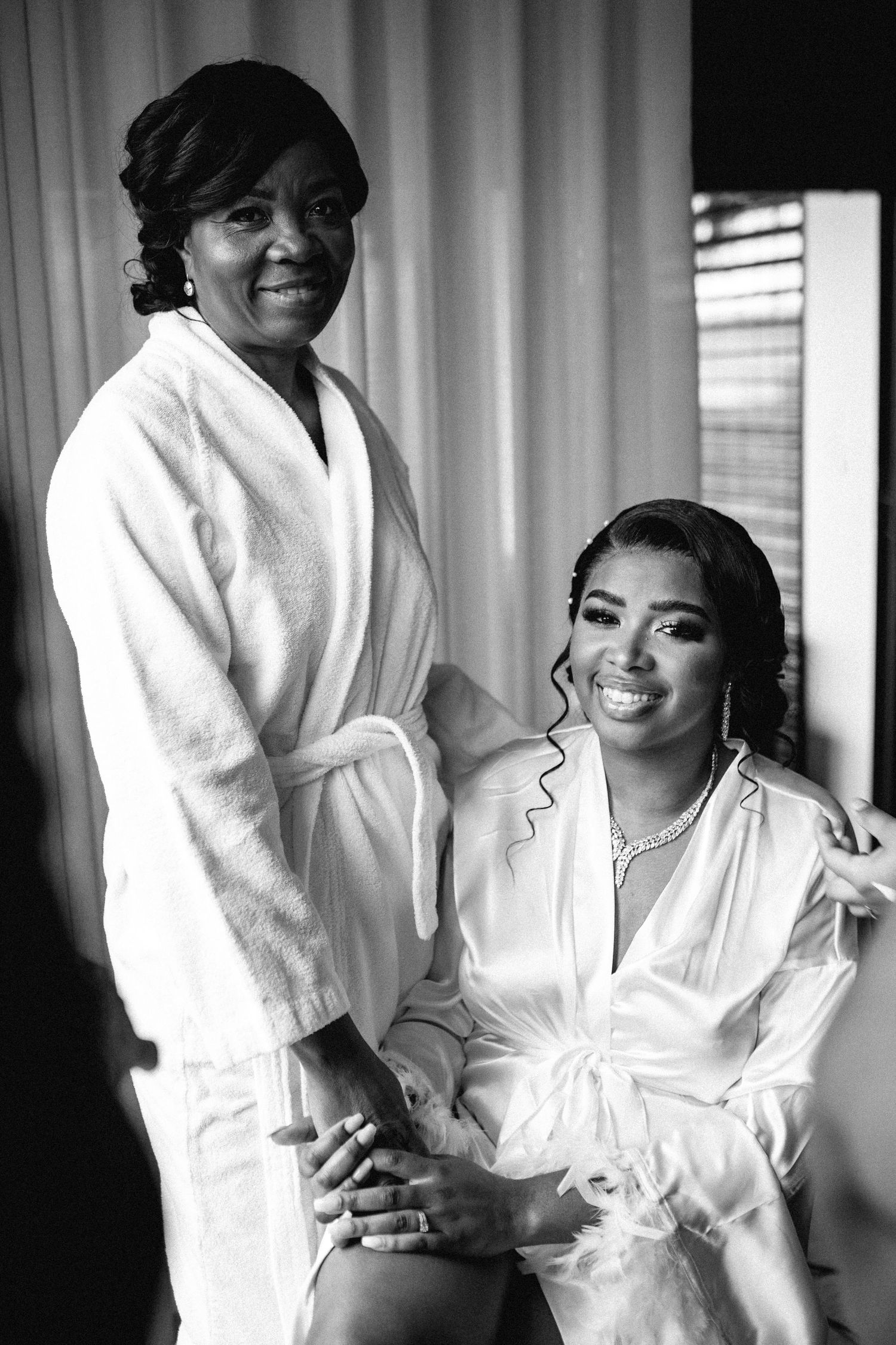 Black and white photos of wedding preparation moments in a bright room with white robes.