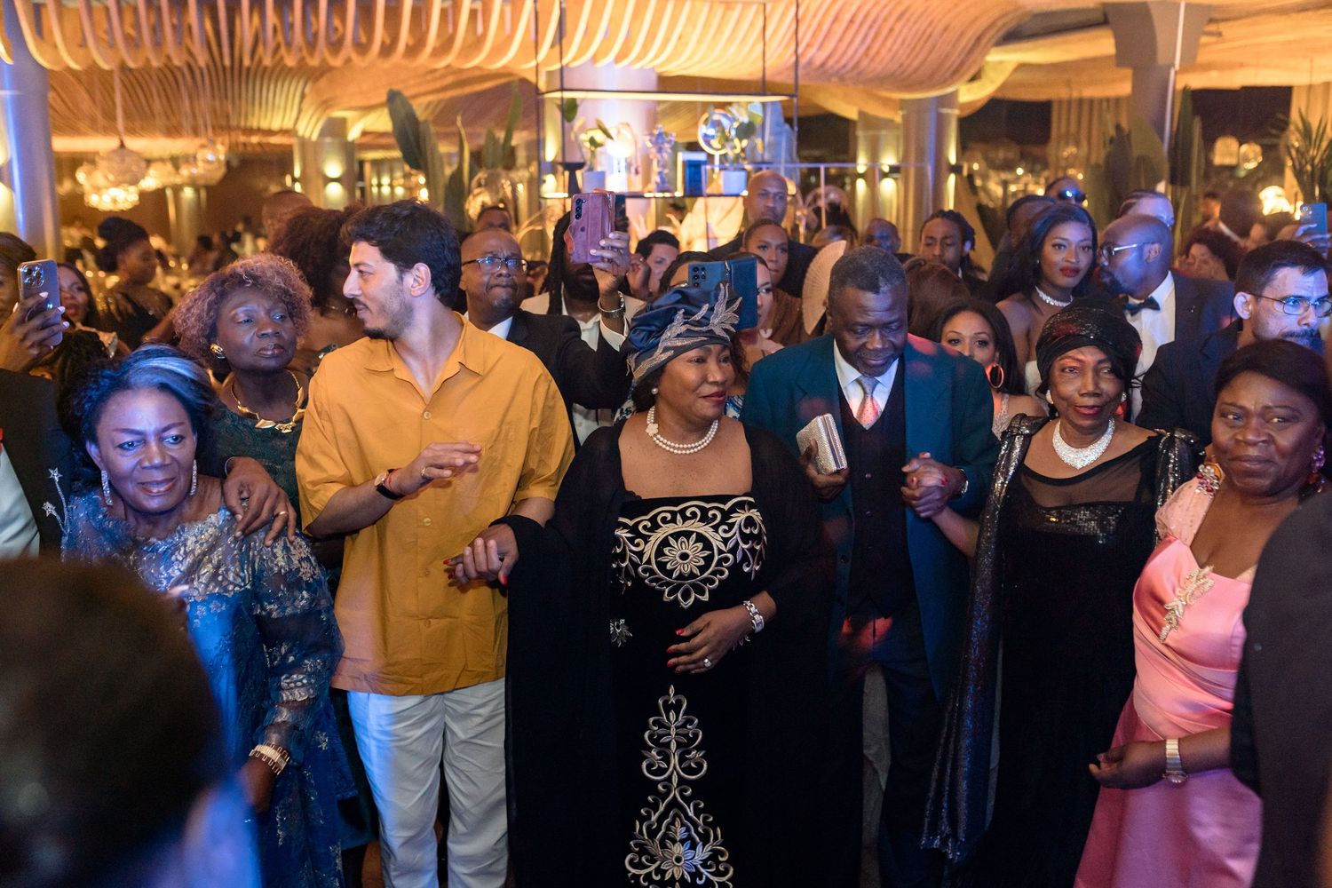 Lively wedding reception with guests dancing and celebrating under warm lighting.