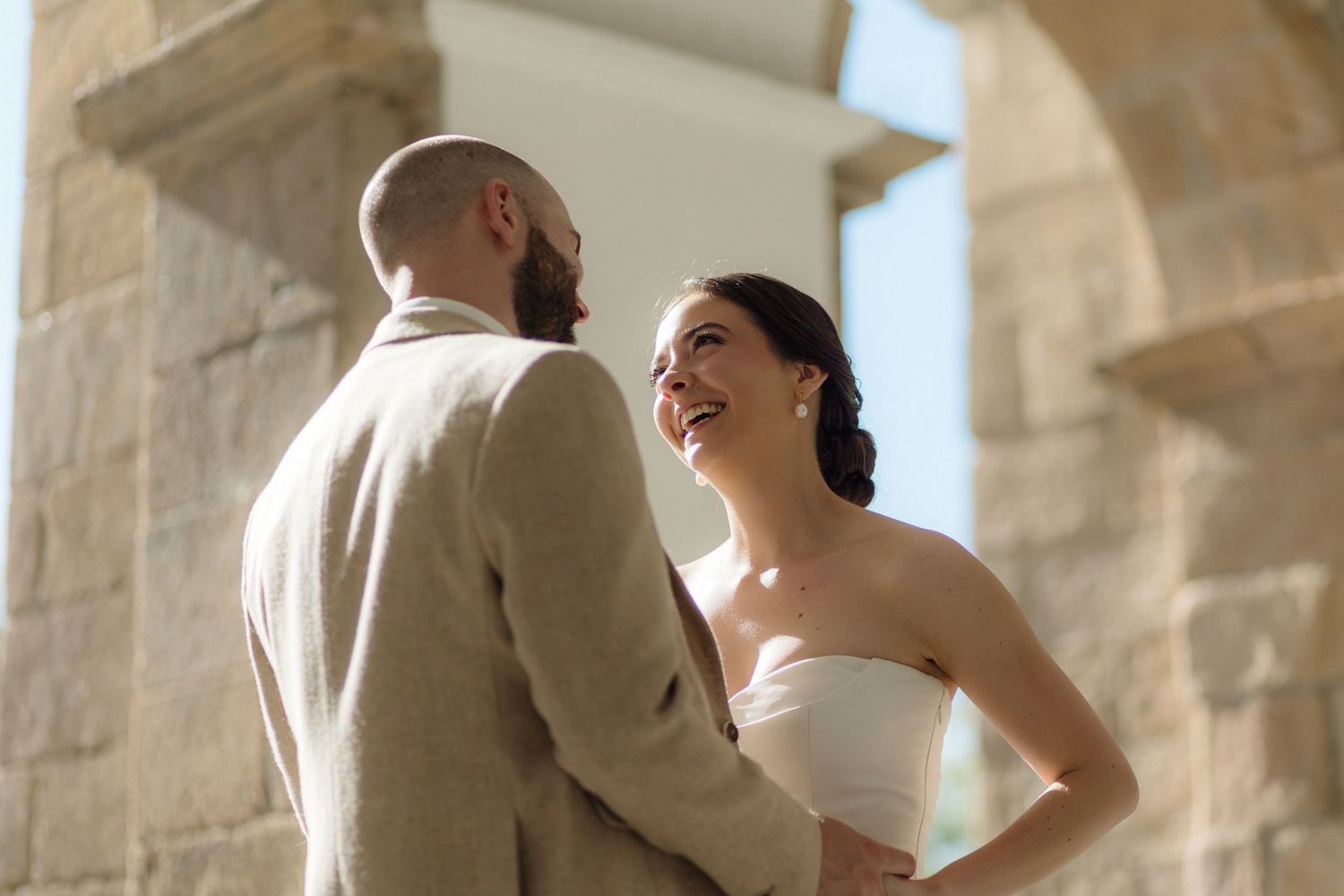 Couple shares romantic moment under stone archway at wedding venue.