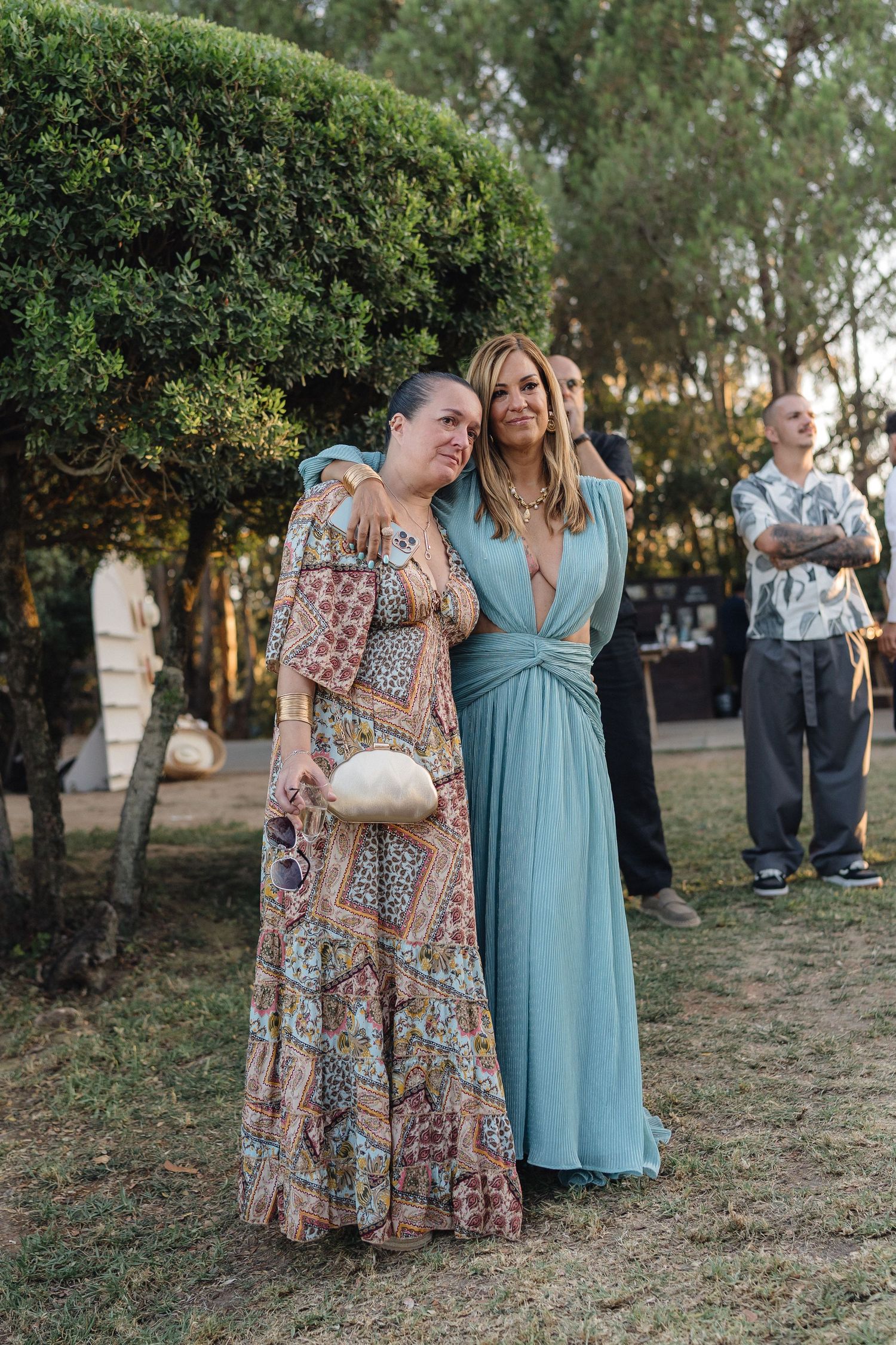 Wedding guests in colorful dresses gather on grassy area during outdoor reception.