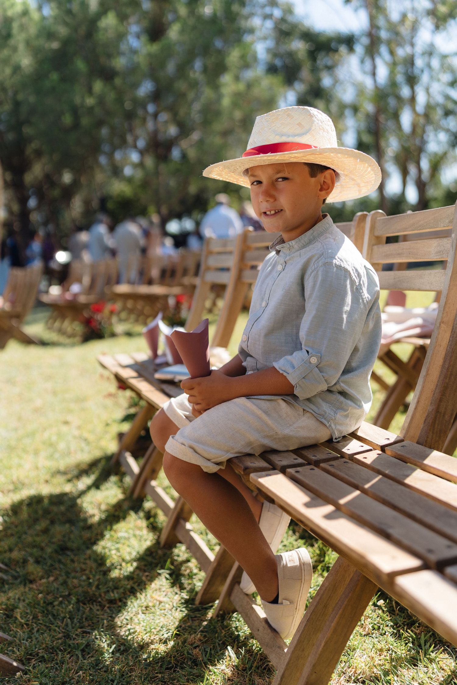 Young attendee in a hat sits on wooden benches during an outdoor event.