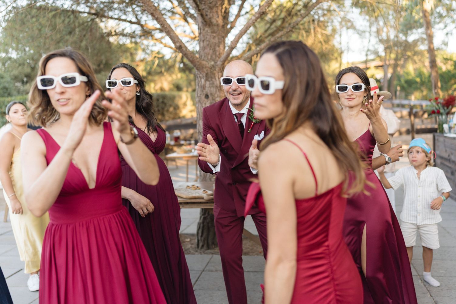 Wedding party in burgundy dresses laughs and celebrates together outdoors.