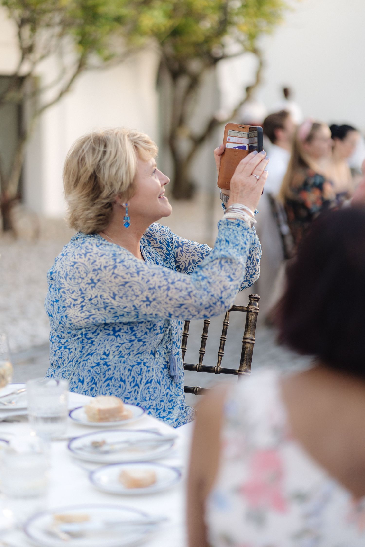 A guest in a blue floral print takes a photo during the reception.