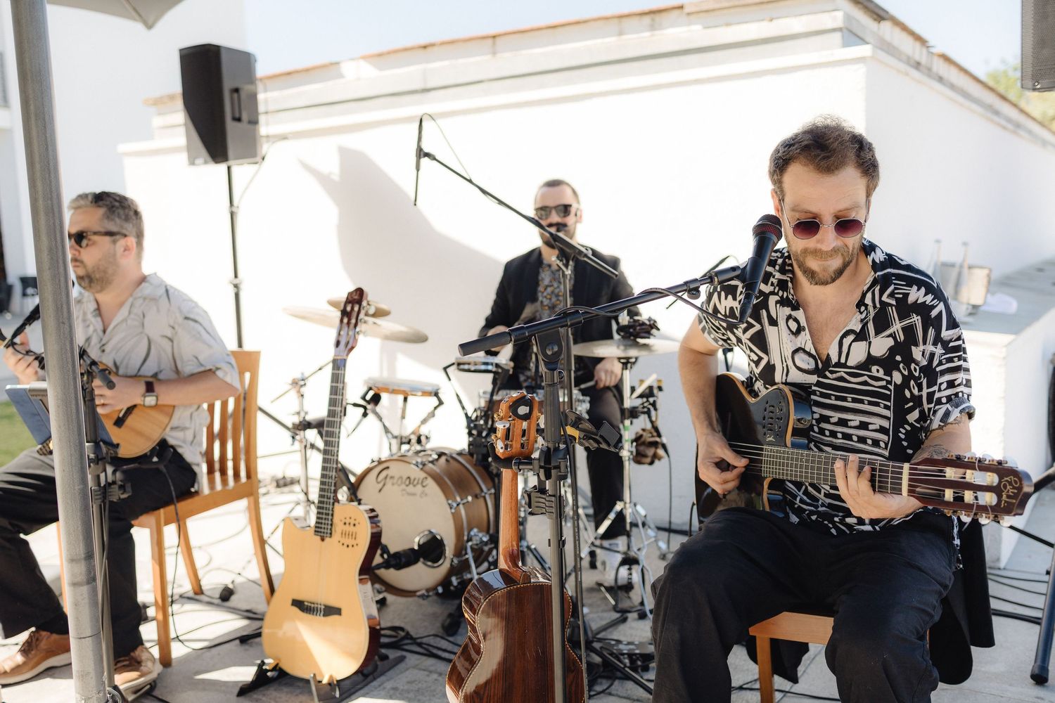 Musicians perform live music at an outdoor event with guitars and drums under a white canopy.
