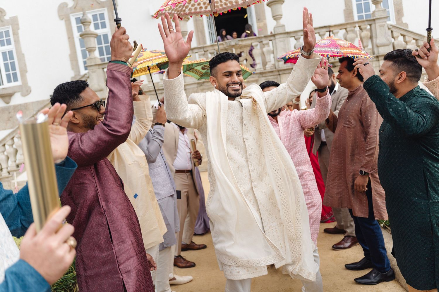 Wedding celebration with guests dancing and celebrating in an elegant white-walled venue.