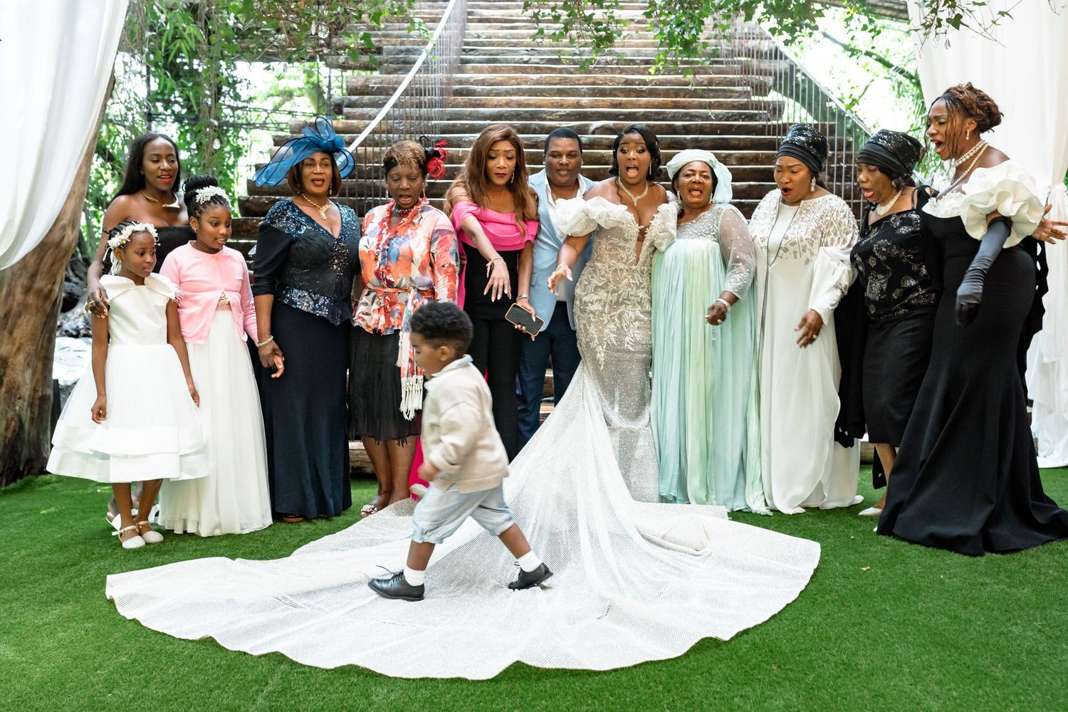 Wedding party and guests gathered on manicured lawn for group photos.
