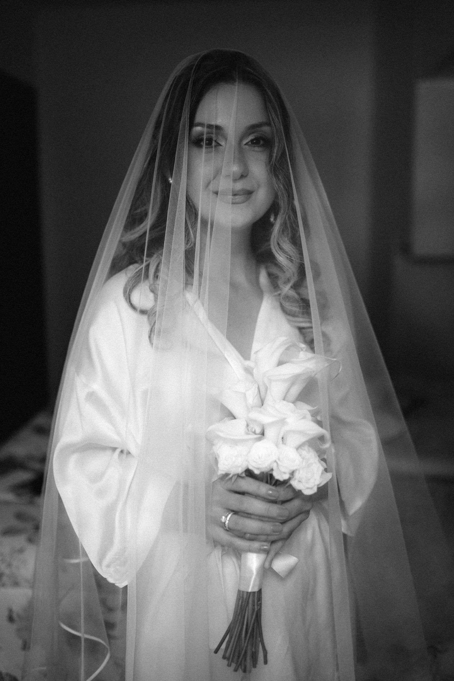 Ethereal black and white bridal portrait with veil and bouquet in dramatic lighting.