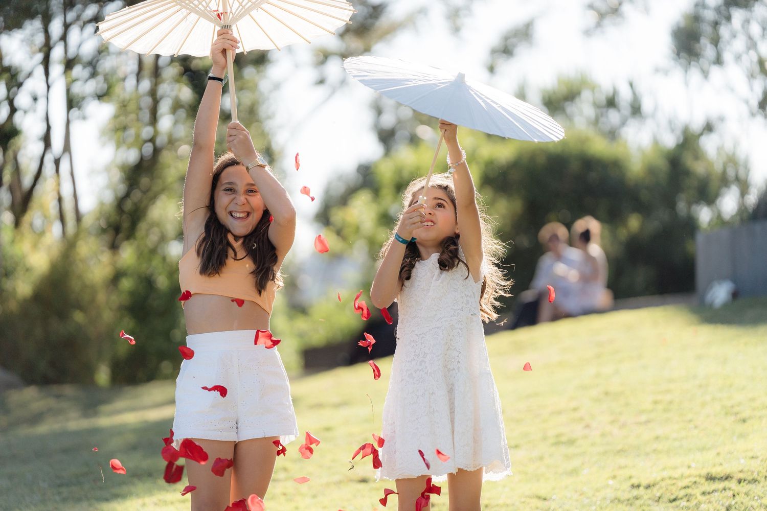 Wedding party in white dresses throws rose petals in celebration during golden hour.