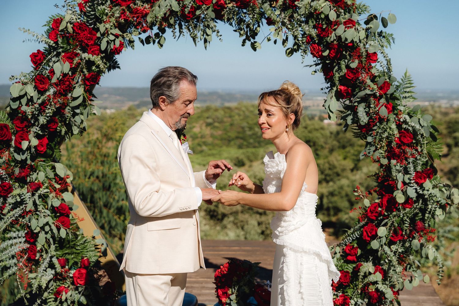 Outdoor wedding ceremony under a stunning red rose floral arch with mountain views.